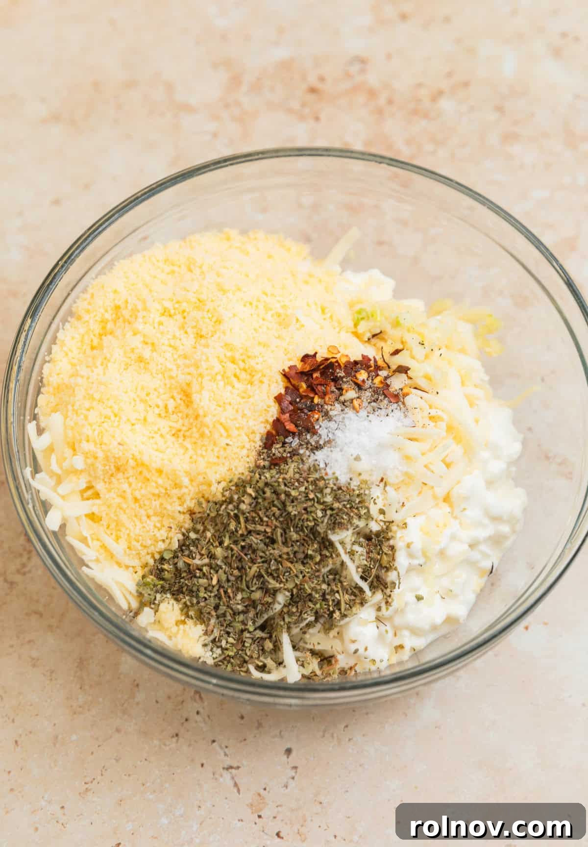 One-Pan Ravioli Lasagna 4 Cottage cheese, parmesan cheese, spices and other ingredients in glass bowl before stirring.