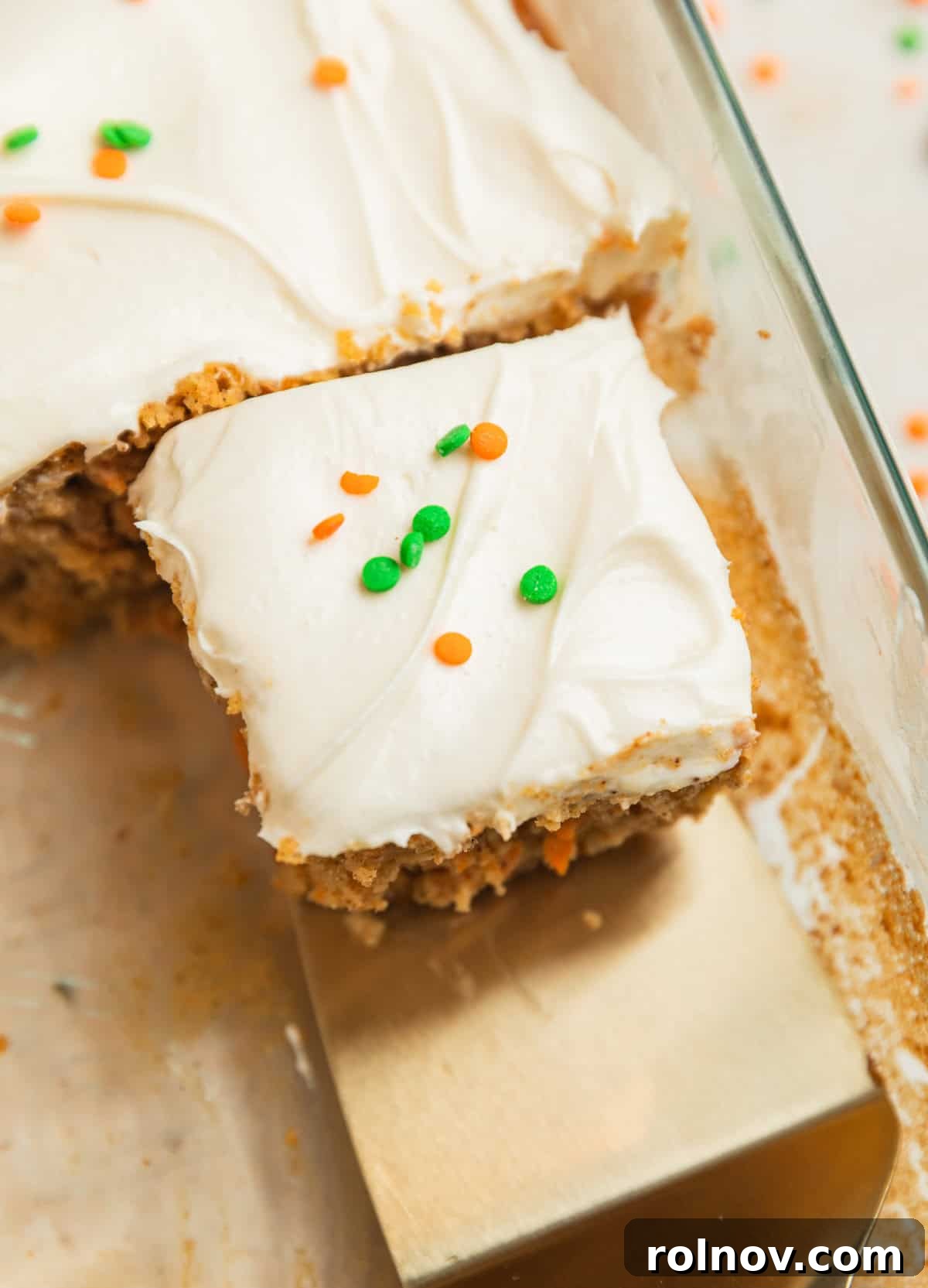 Foolproof Box Mix Carrot Cake 2 A perfectly sliced piece of carrot cake, generously topped with cream cheese frosting and festive orange and green sprinkles, resting in a baking pan.