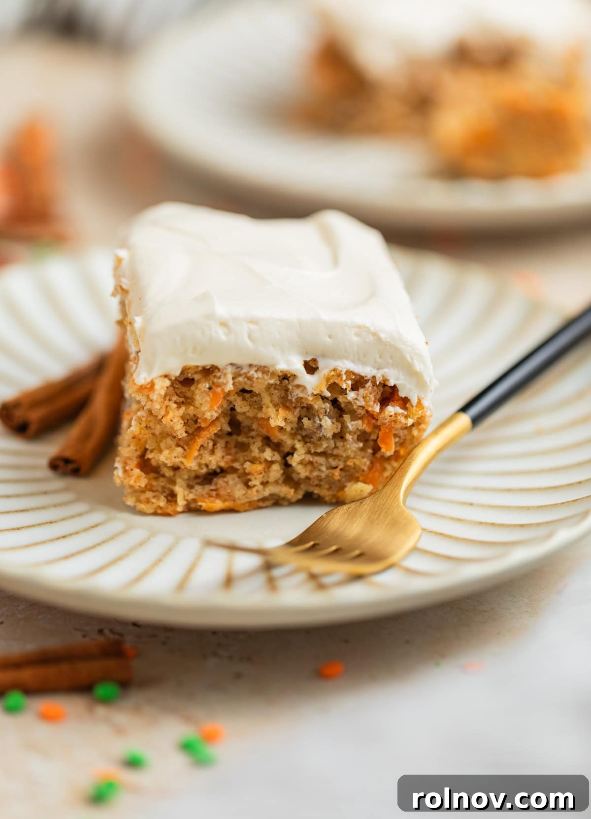 Foolproof Box Mix Carrot Cake 12 A beautiful slice of carrot cake, topped with creamy frosting, served on a white plate with a fork and decorative cinnamon sticks beside it, highlighting its rich texture.