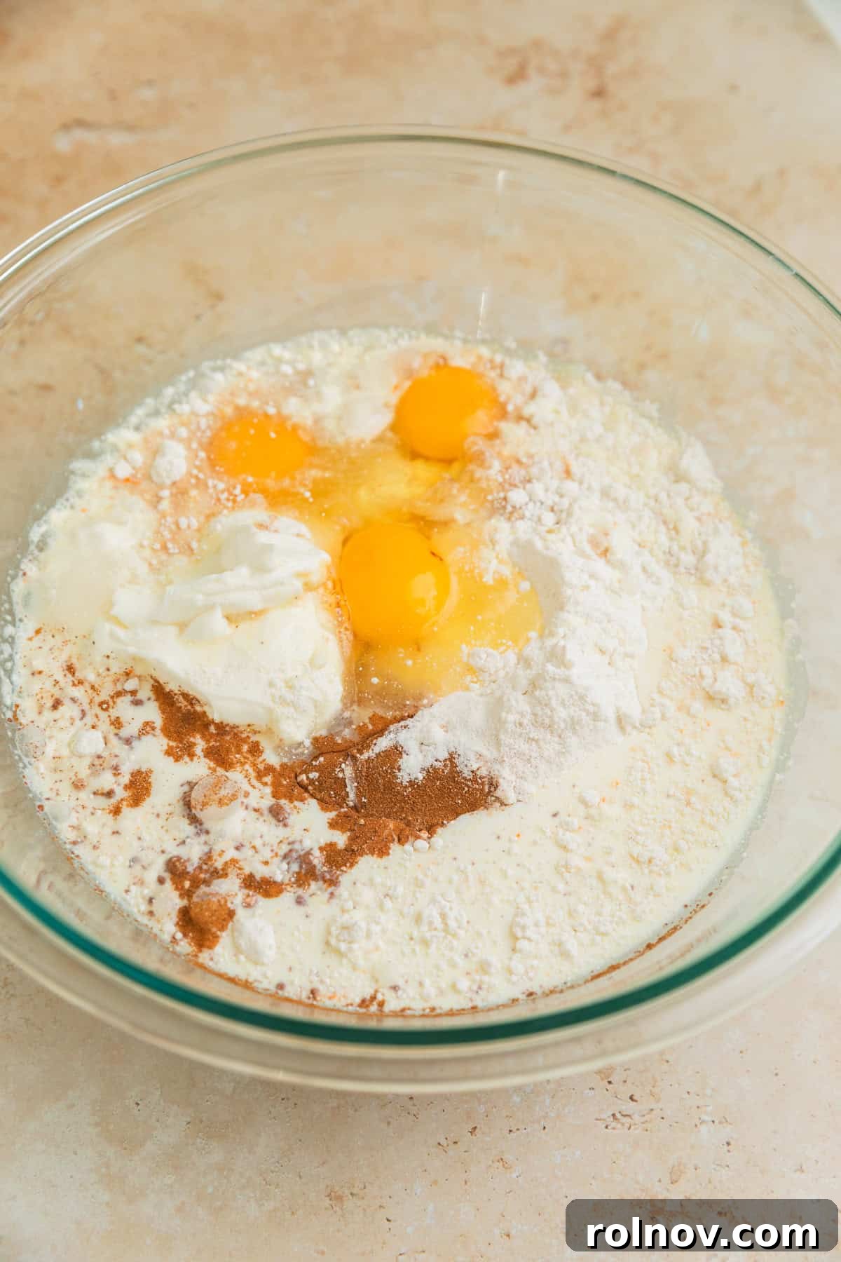 Foolproof Box Mix Carrot Cake 4 Yellow cake mix, milk, eggs, oil, sour cream, cinnamon, and nutmeg gathered in a large glass bowl, ready for mixing to form the cake batter.