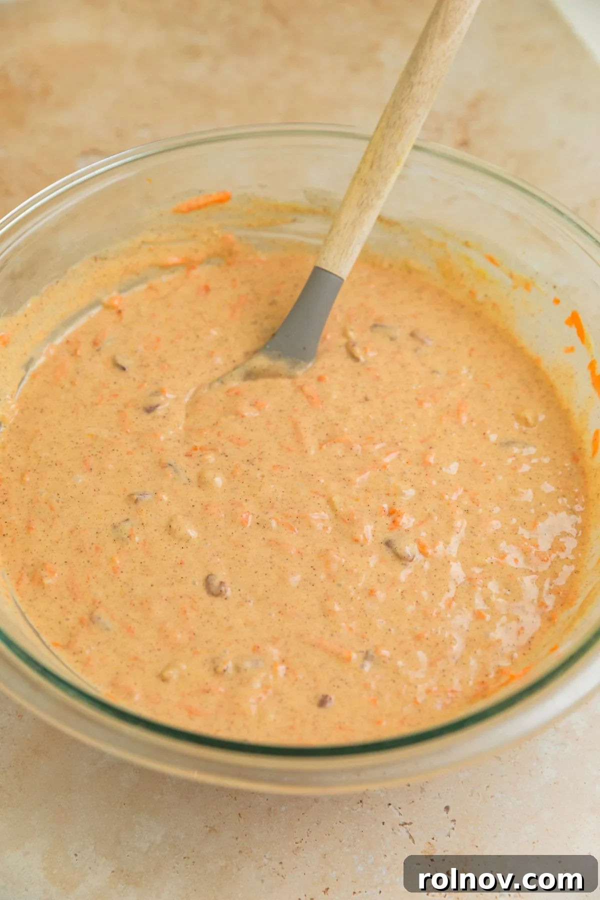 Foolproof Box Mix Carrot Cake 7 Fully mixed carrot cake batter, rich with shredded carrots, pecans, and pineapple, in a bowl with a spoon, ready for baking.