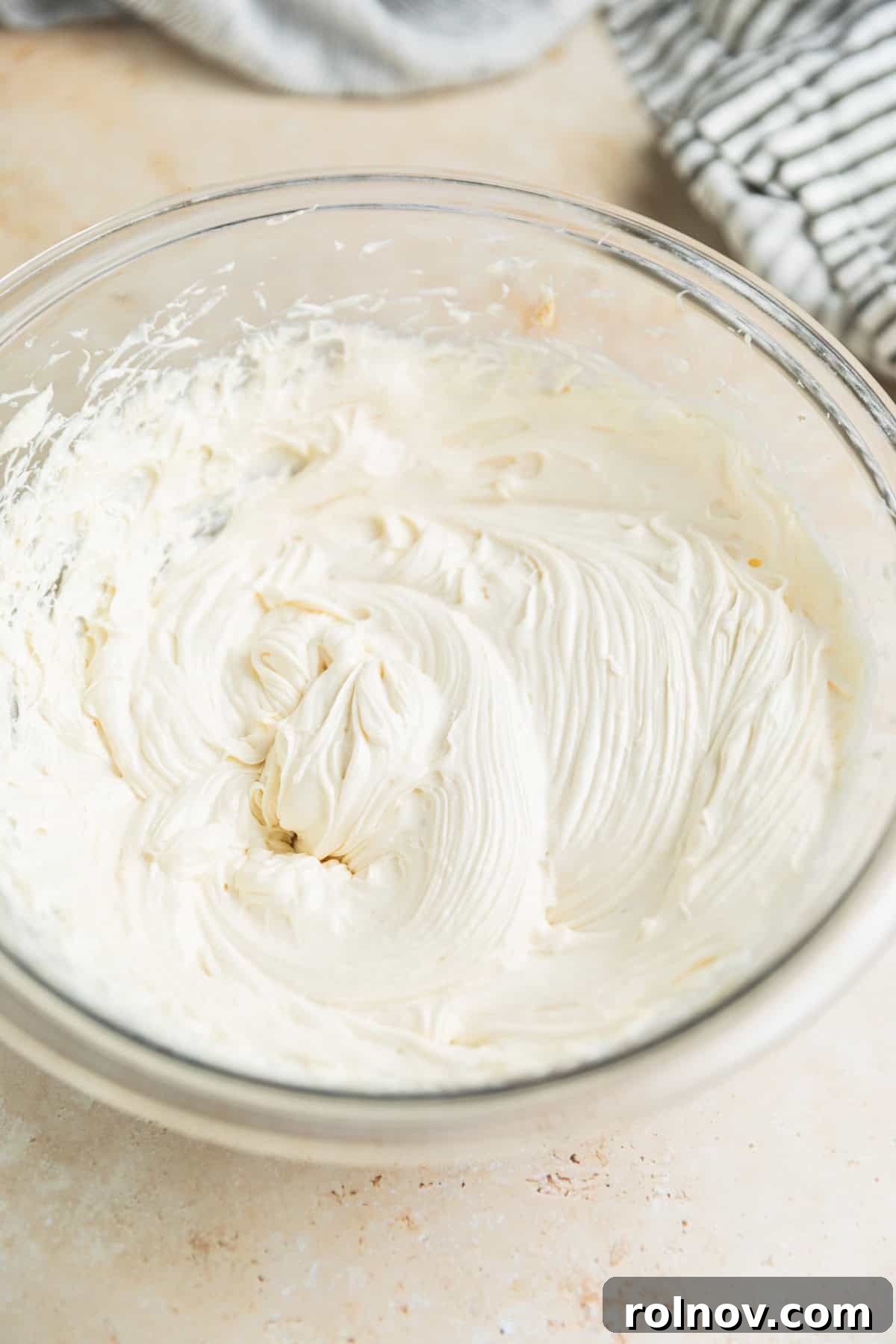 Foolproof Box Mix Carrot Cake 10 Cream cheese frosting being whipped vigorously with softened cream cheese and brown sugar in a glass bowl using an electric mixer, creating a smooth, creamy texture.