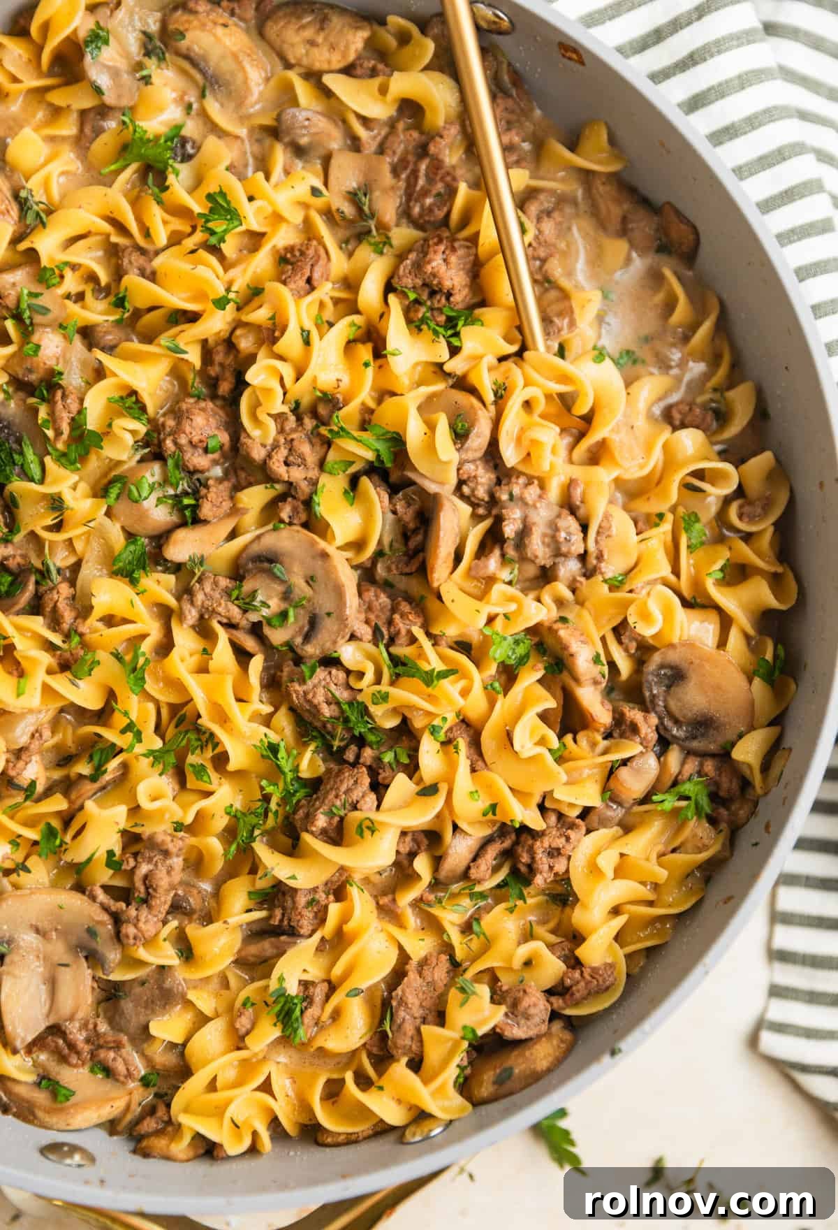 Creamy One-Pot Ground Beef Stroganoff 2 Skillet with one pot ground beef stroganoff topped with chopped parsley and serving spoon scooping in to the skillet.