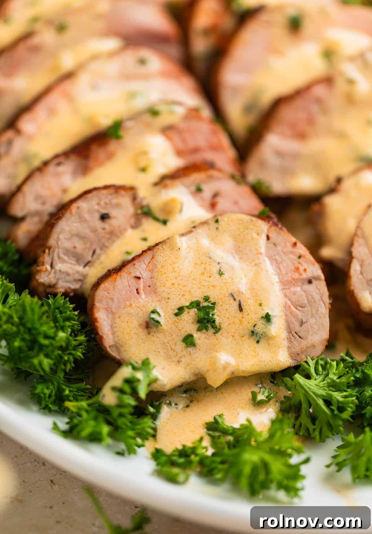 Seared Pork Tenderloin with Dijon Cream 2 Roasted pork tenderloin sliced on plate with creamy mustard sauce poured over top.