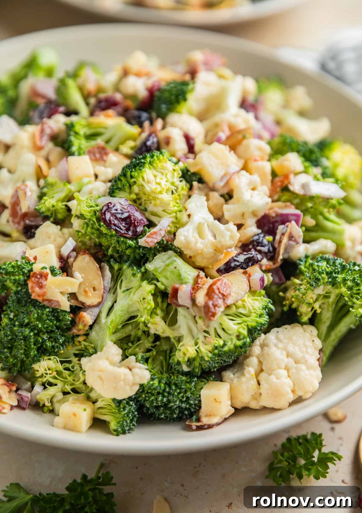Vibrant Broccoli Cauliflower Medley 2 Delicious broccoli and cauliflower salad with cranberries, almonds, cheese, and crispy bacon in a large serving bowl, ready to be enjoyed.