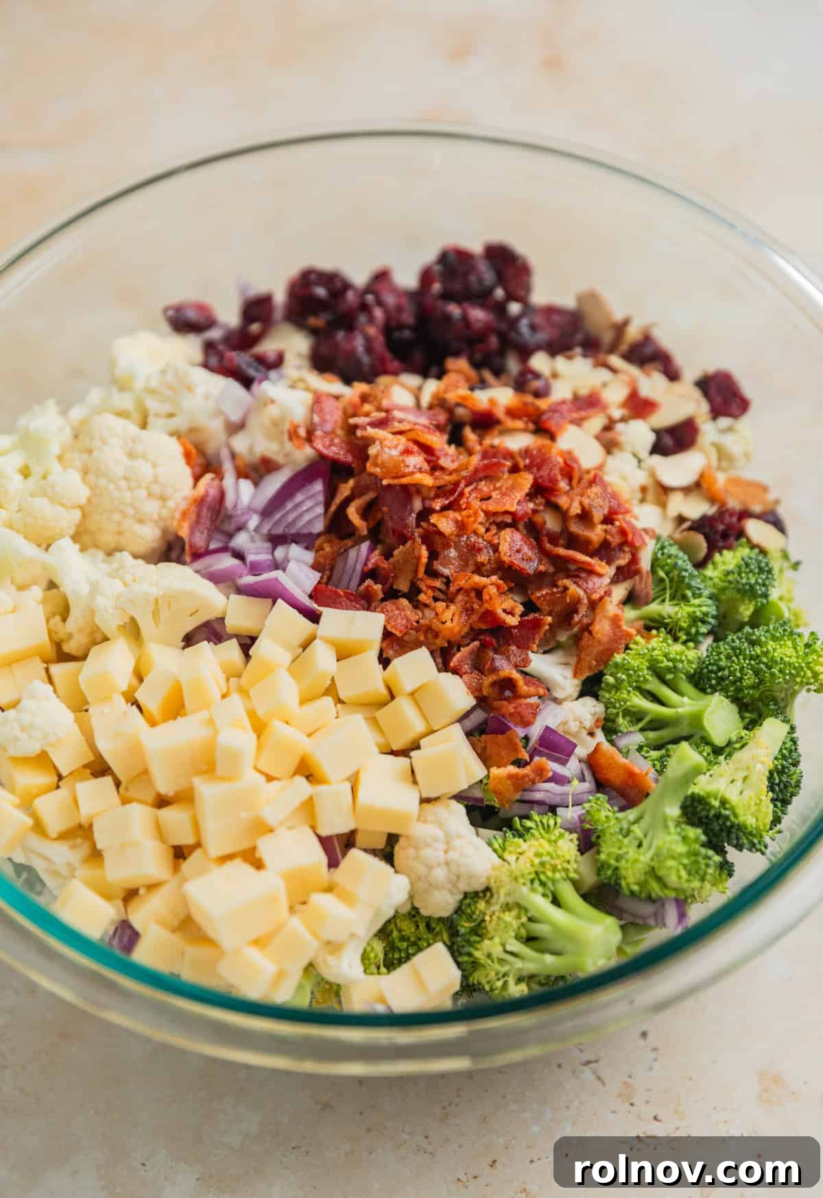 Vibrant Broccoli Cauliflower Medley 4 A glass bowl filled with bite-sized broccoli and cauliflower florets, crispy bacon, small cubes of cheese, and other vibrant ingredients, all ready for mixing.