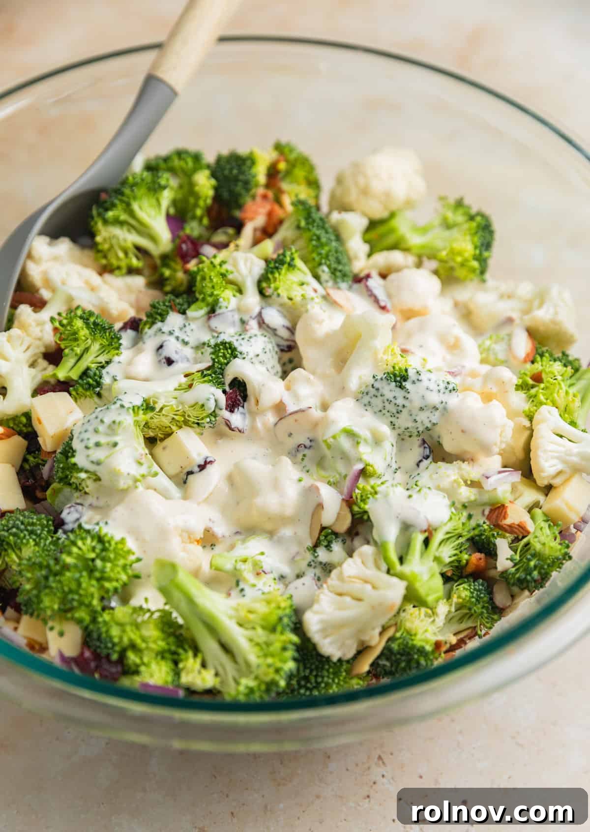 Vibrant Broccoli Cauliflower Medley 7 Creamy dressing being poured directly over the mixed broccoli and cauliflower salad ingredients in a large bowl.