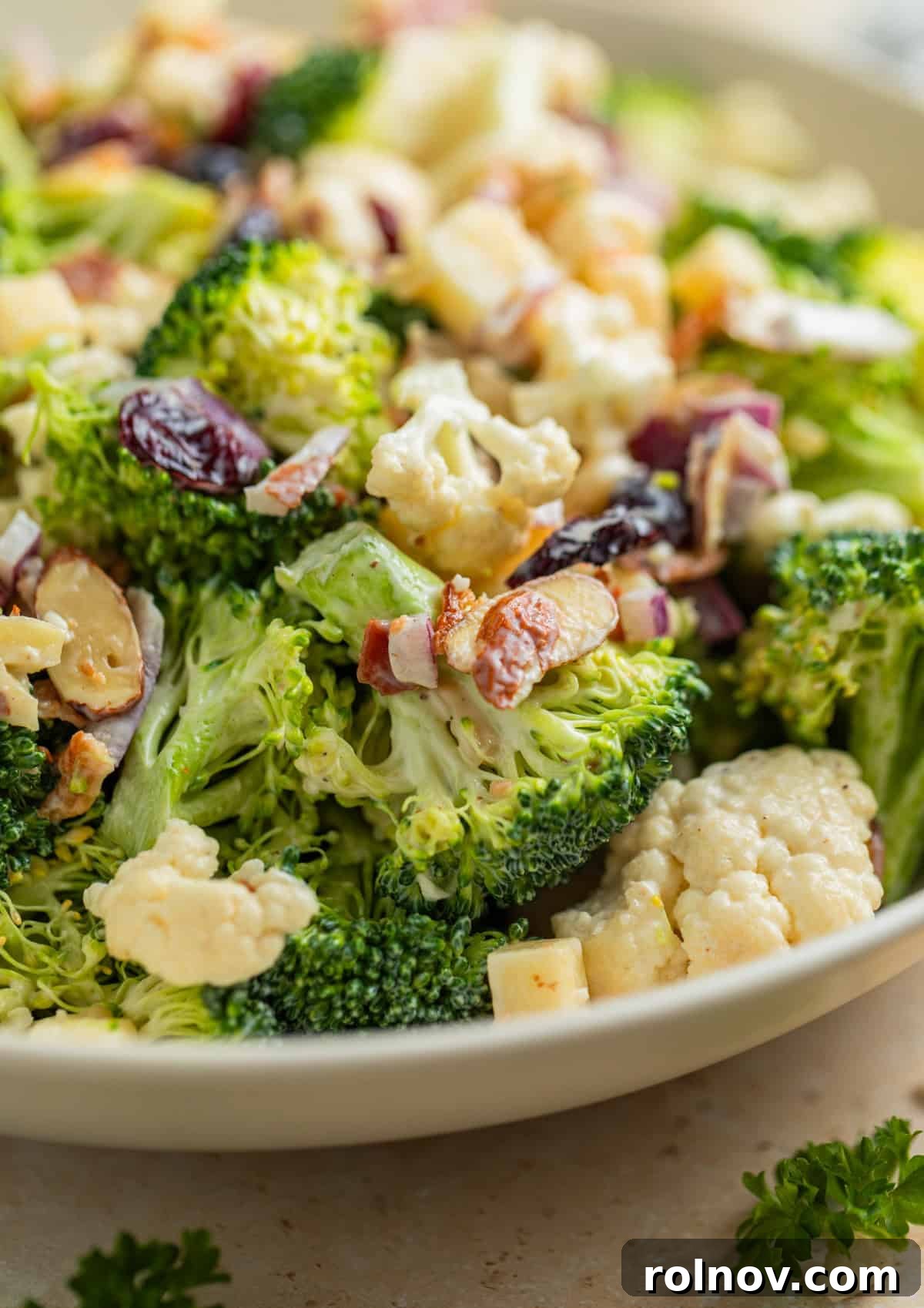 Vibrant Broccoli Cauliflower Medley 9 A beautifully presented serving dish filled with broccoli and cauliflower salad, garnished with extra chopped bacon, dried cranberries, and sliced almonds on top.