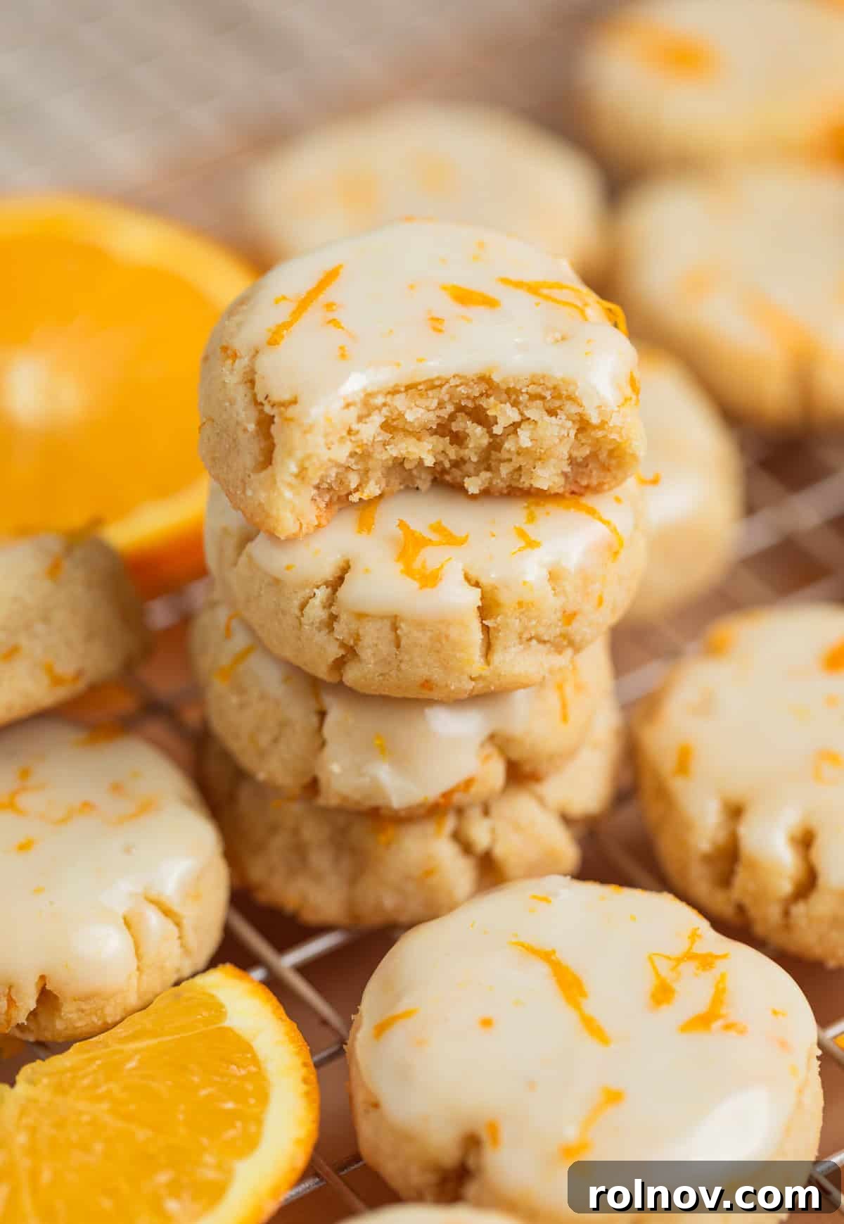 Stack of beautifully iced orange almond flour cookies, with a tempting bite taken out of the top cookie, showcasing its soft, chewy interior.