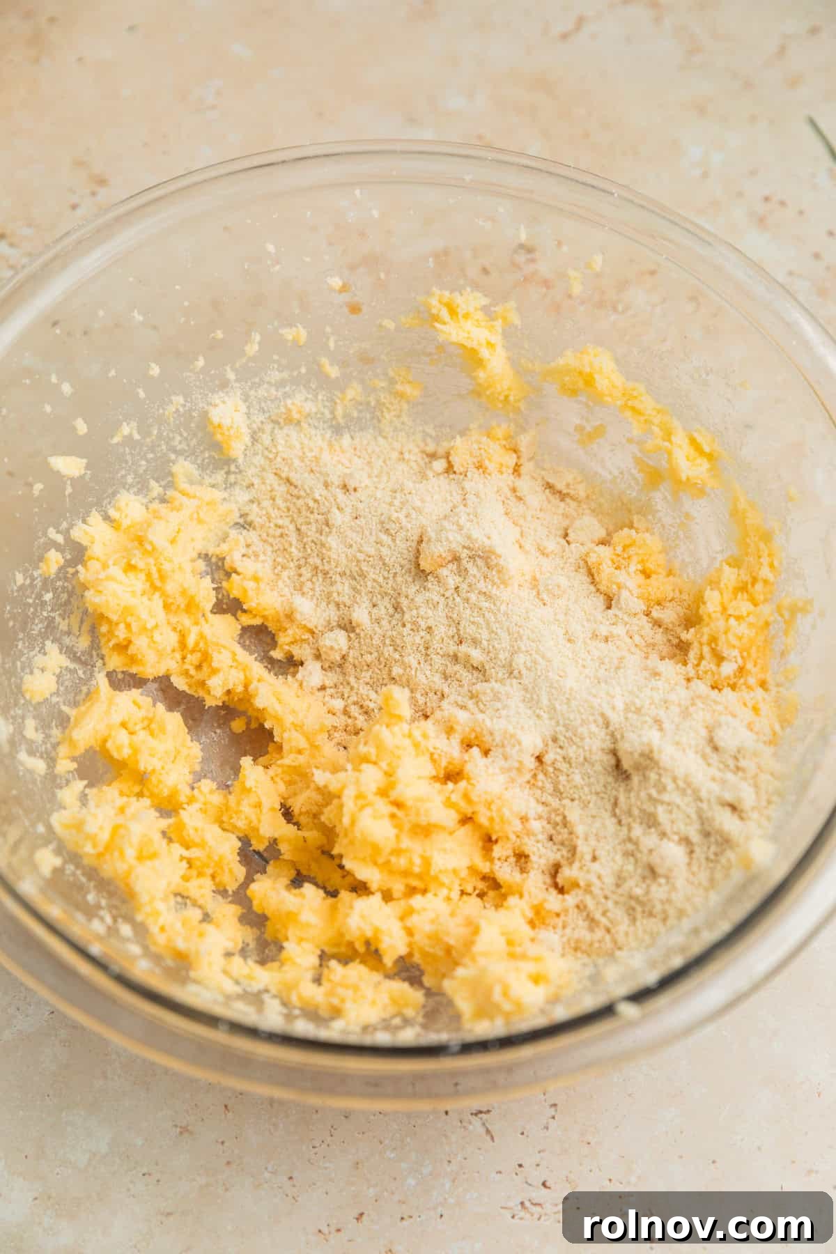 Finely ground almond flour being gradually added to the creamed butter and sugar mixture in a glass mixing bowl, creating a developing dough.