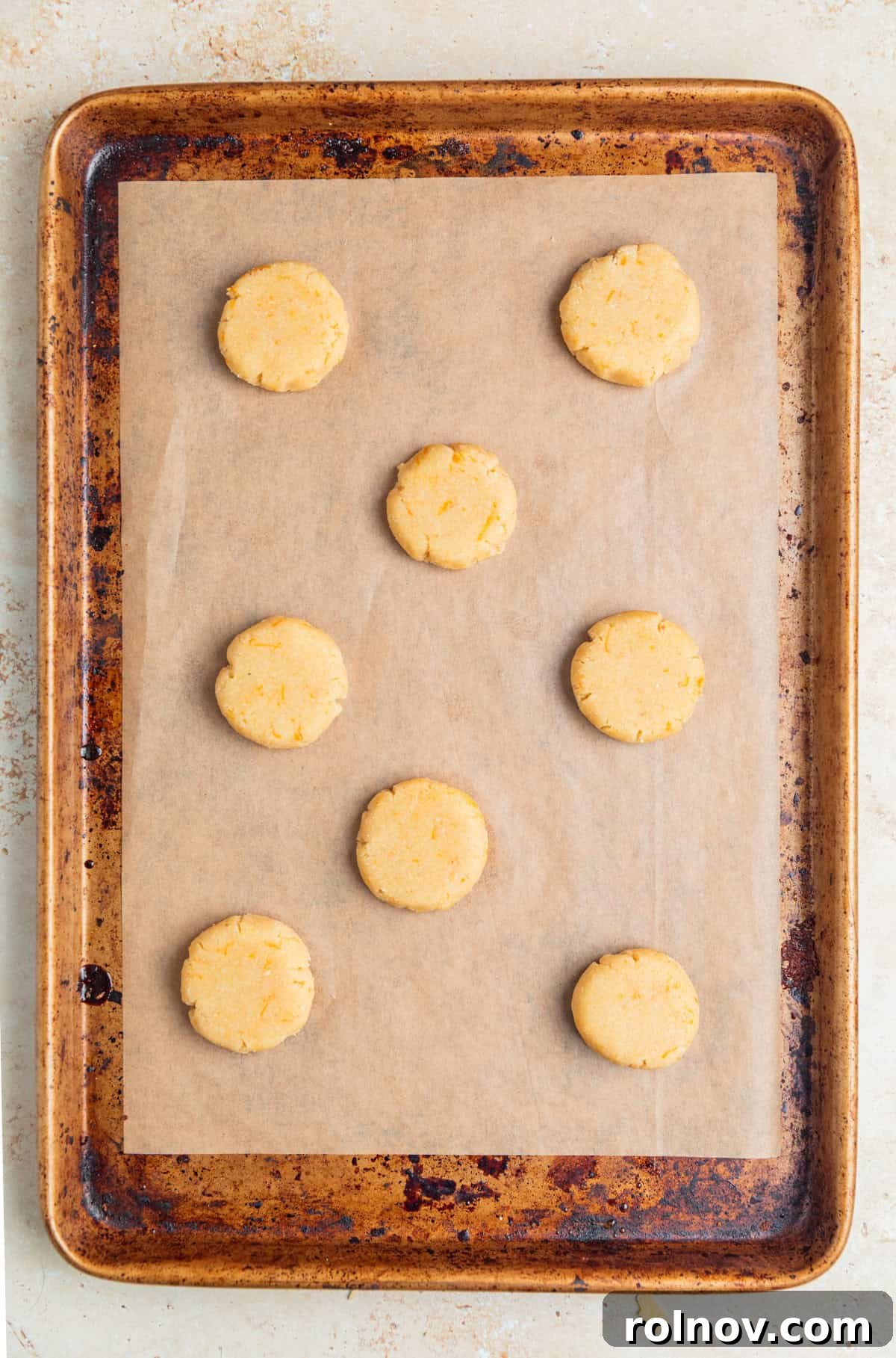 Evenly spaced, flattened balls of orange almond flour cookie dough arranged on a parchment-lined cookie sheet, ready for baking.