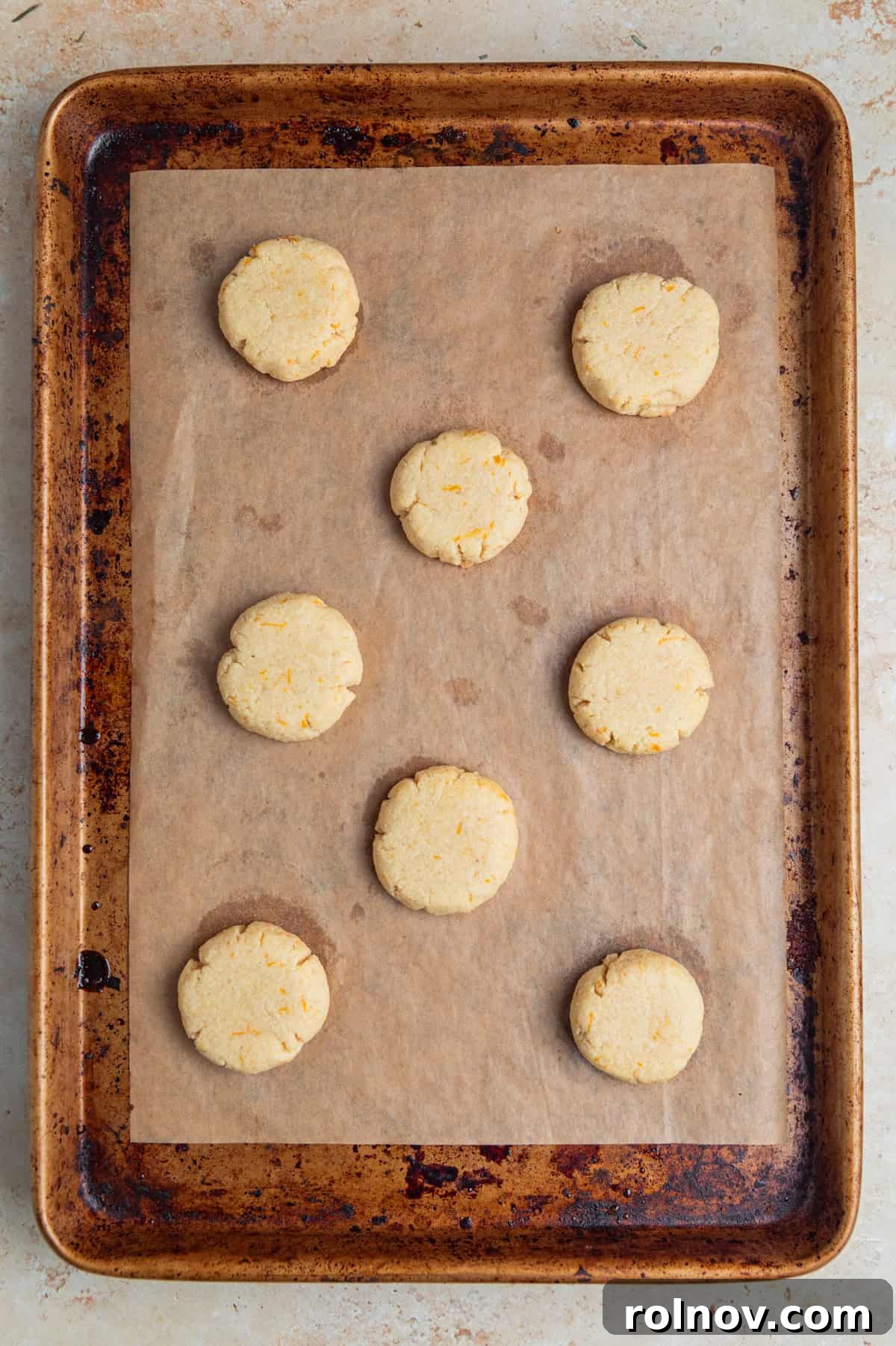 Freshly baked orange almond flour cookies cooling on a parchment-lined baking pan, displaying light golden-brown edges and a slightly textured surface.