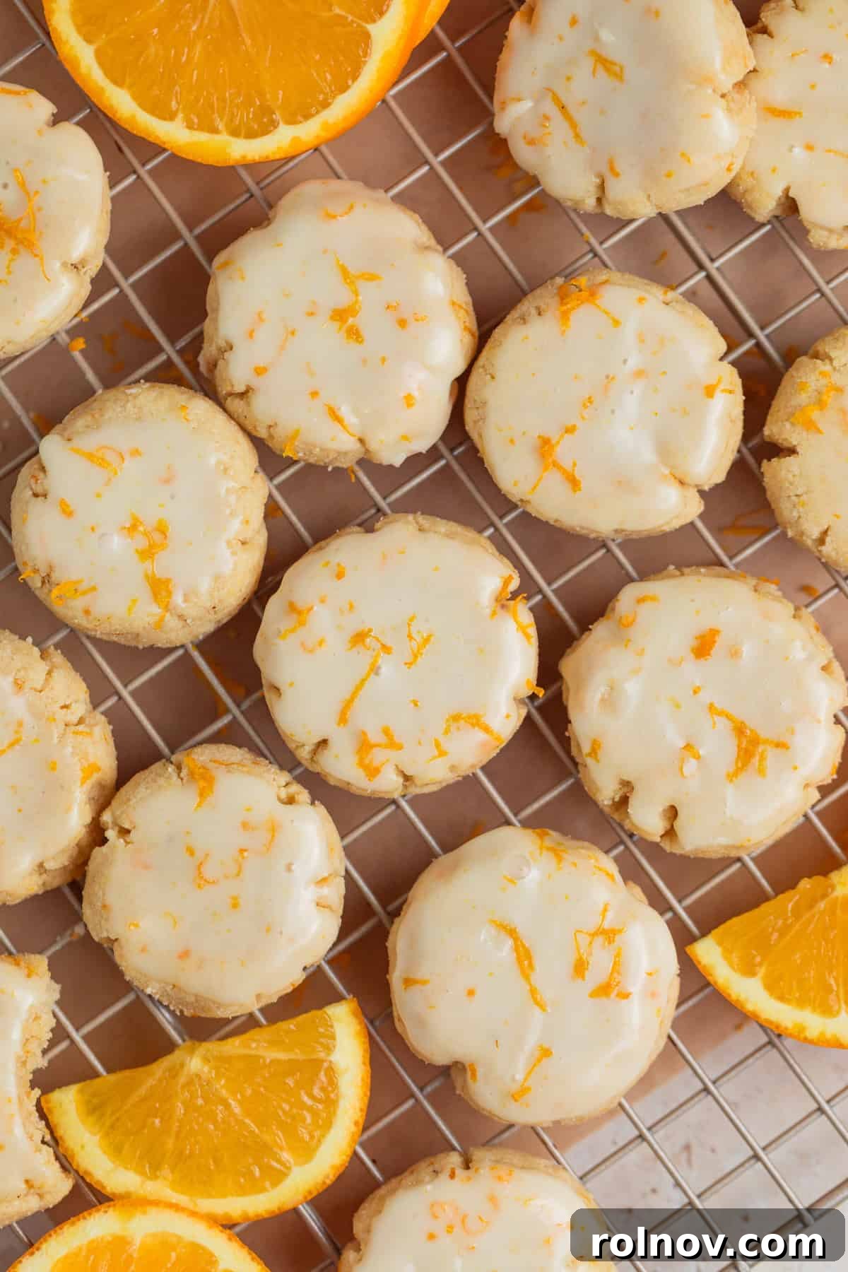 An overhead view of numerous freshly iced orange cookies arranged neatly on a wire cooling rack, with some garnished with additional zest.
