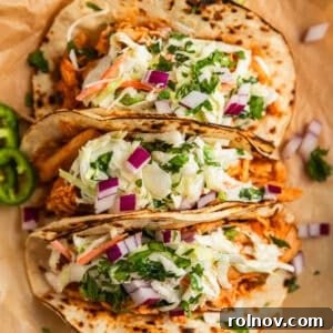 Fall-Apart BBQ Chicken Tacos with Zesty Slaw 11 BBQ chicken tacos topped with slaw and chopped cilantro and red onion on parchment.