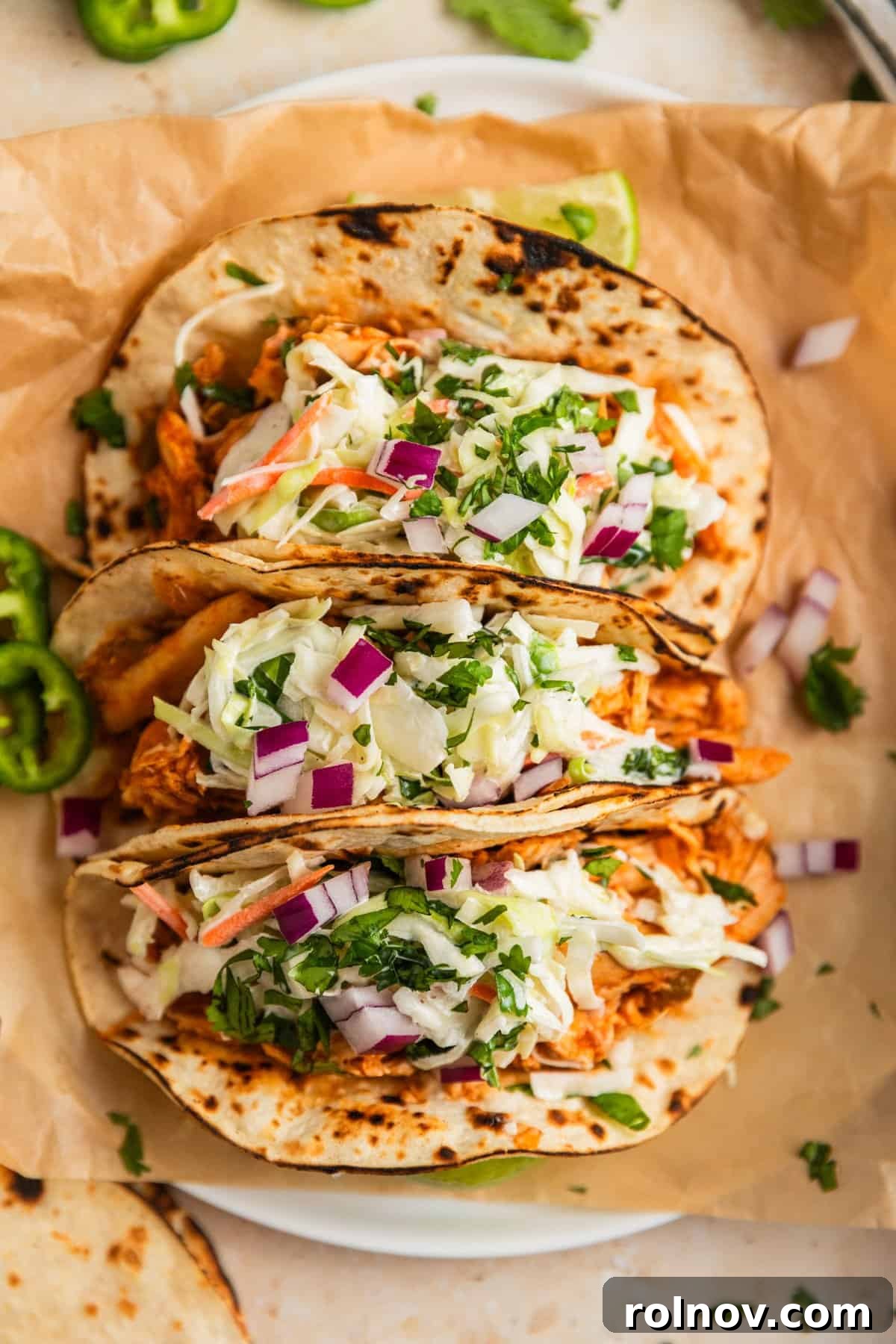 Fall-Apart BBQ Chicken Tacos with Zesty Slaw 10 Three chicken tacos on parchment topped with cole slaw.