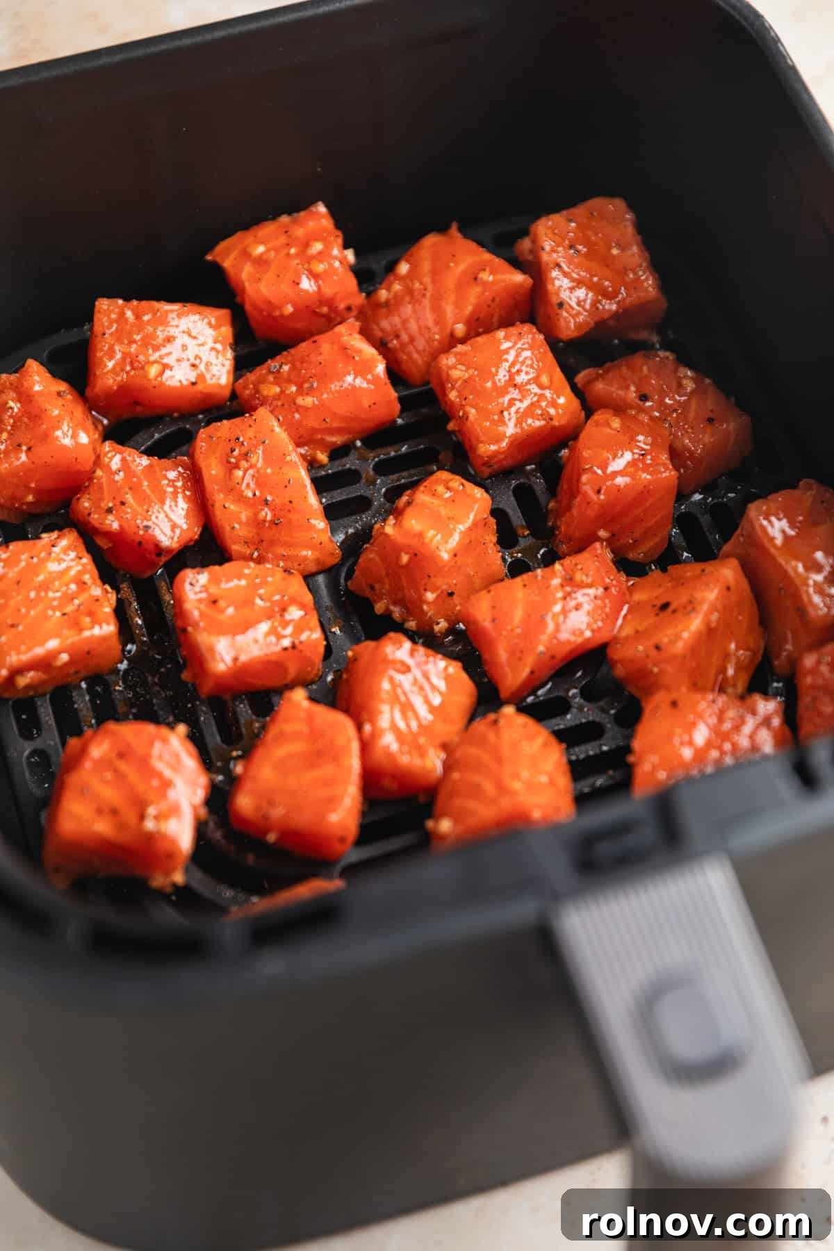 Crispy Air Fryer Salmon Bites 6 Raw salmon bites in air fryer basket before cooking.