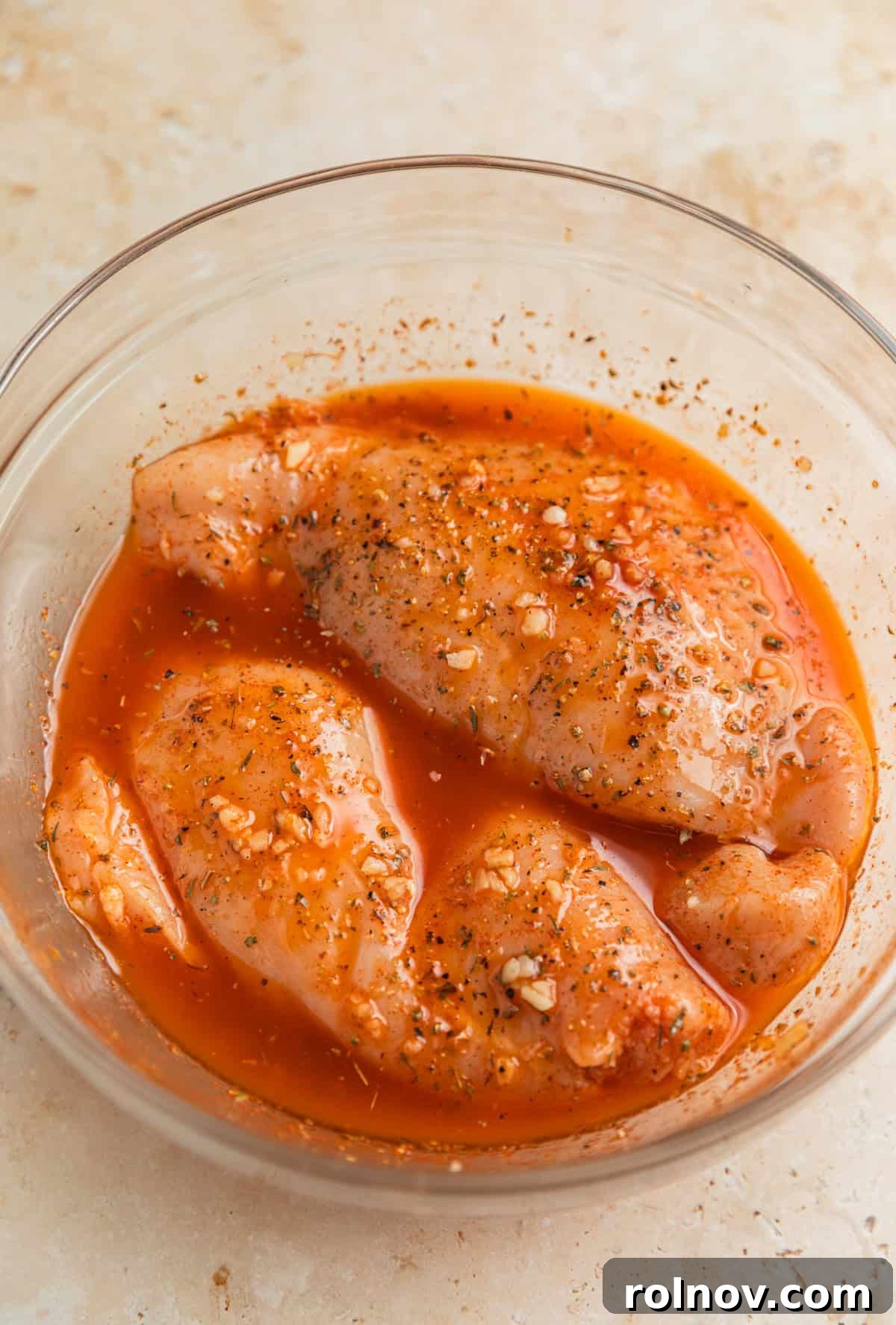 Chicken breast in marinade in glass bowl.