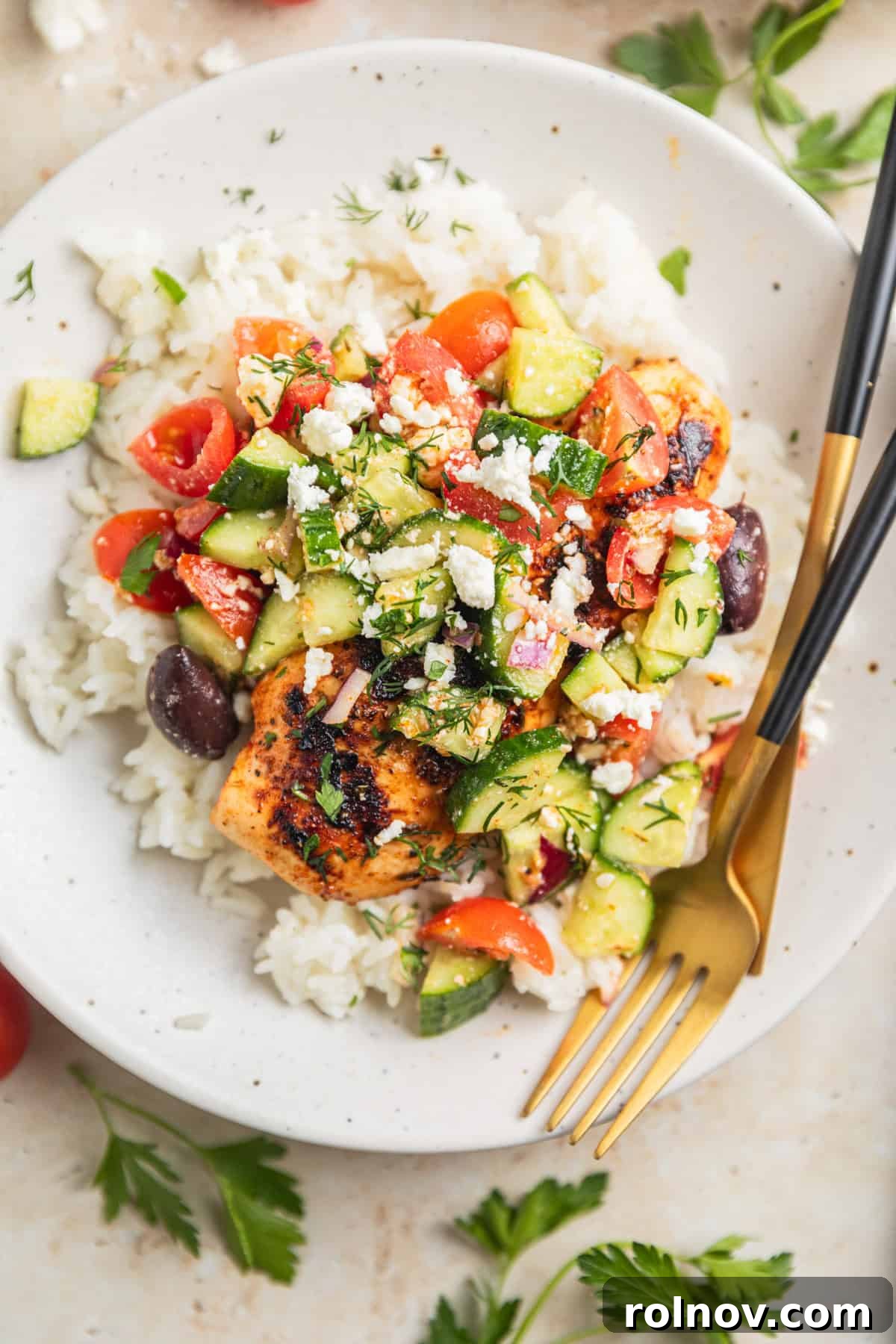 Grilled chicken on plate over rice topped with cucumbers, feta, olives and dill.