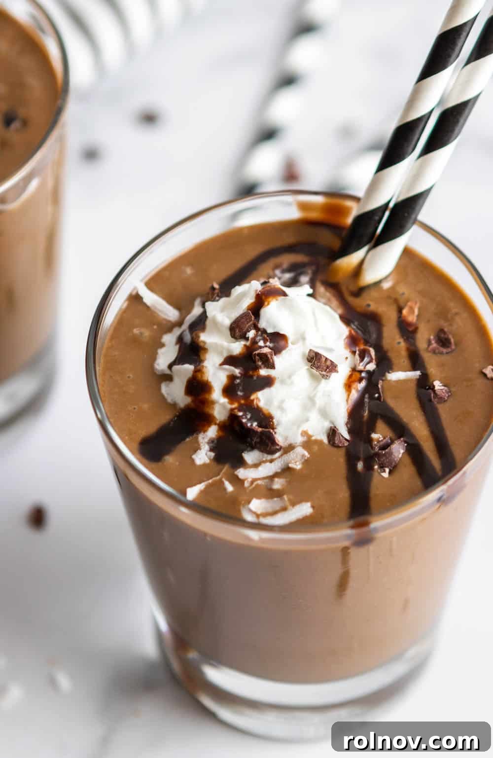 Creamy Almond Joy Smoothie in a glass, topped with whipped cream, cacao nibs, and straws.