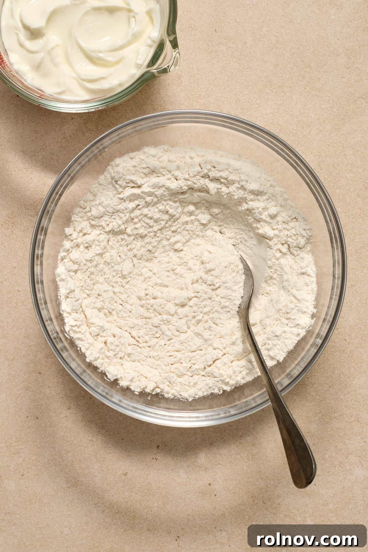 Combining Dry Ingredients for Bagel Dough Dry ingredients including flour, baking powder, and salt, are measured into a glass mixing bowl, ready for whisking.