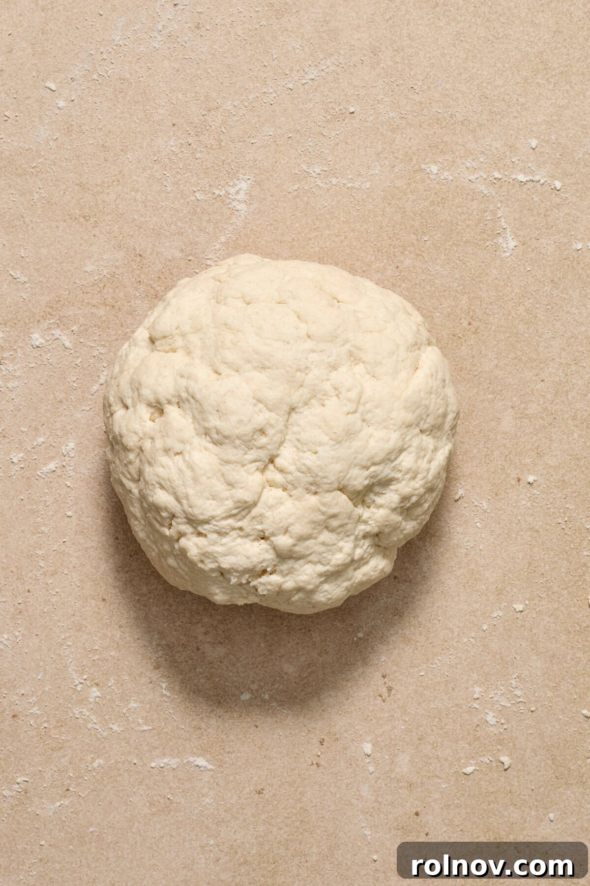 Kneading the Bagel Dough A smooth ball of Greek yogurt bagel dough rests on a lightly floured surface, ready for kneading.