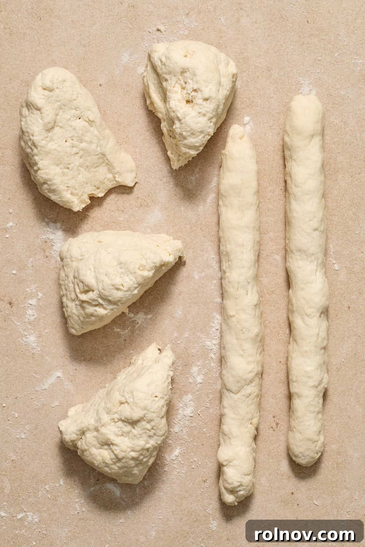 Shaping Bagel Ropes A long, thin rope of Greek yogurt bagel dough on a floured surface, shaped from one of the divided portions.