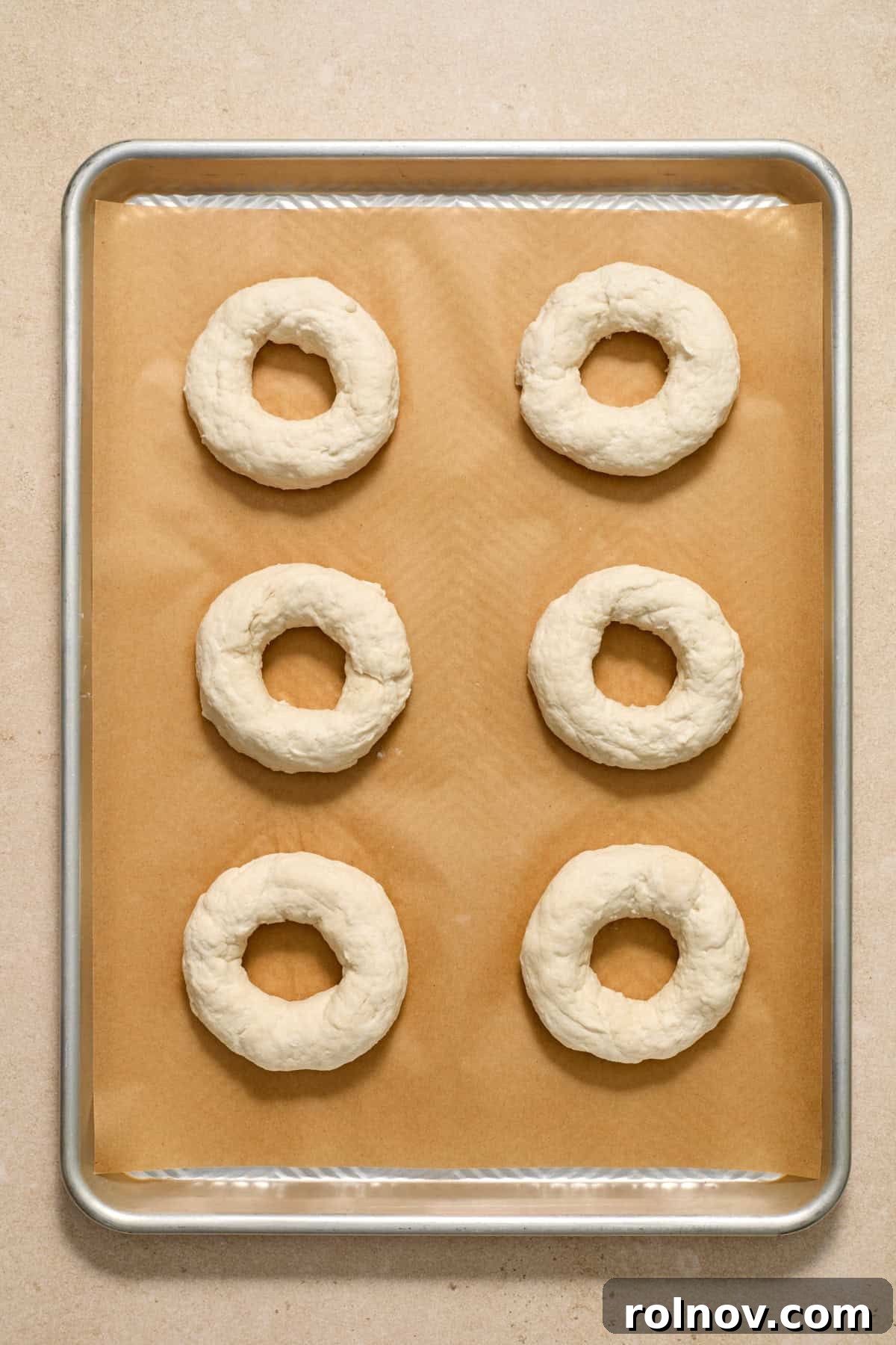 Bagels Ready for Baking Six perfectly formed Greek yogurt bagels arranged neatly on a parchment paper-lined cookie sheet, ready for the egg wash.