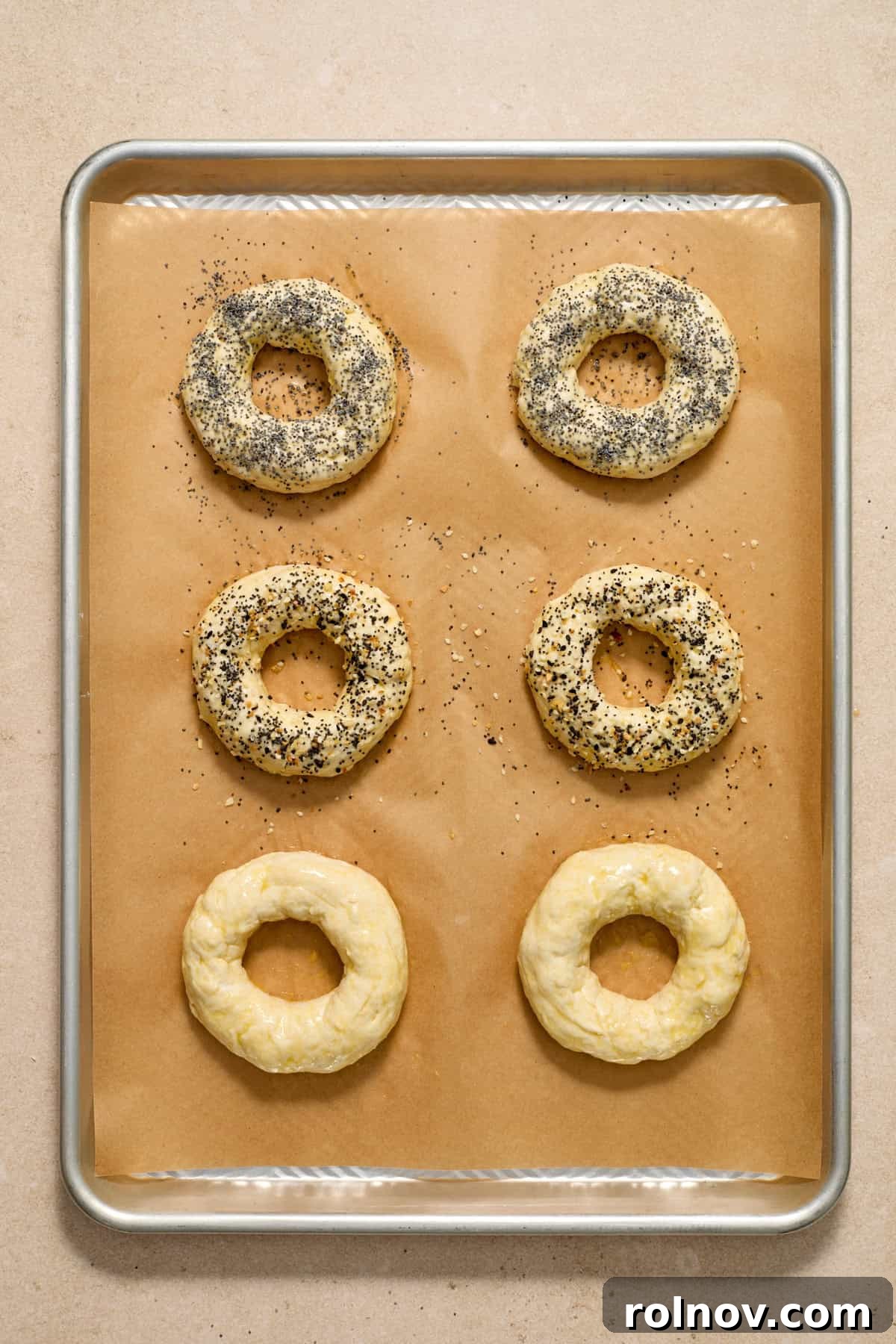 Applying Egg Wash and Toppings to Bagels Bagels on a baking sheet, brushed with egg wash and generously topped with poppy seeds and other seasonings before baking.