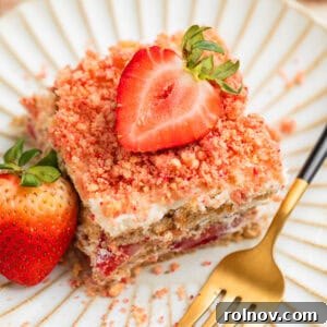 Layered strawberry icebox cake topped with strawberry crunch on plate with fresh strawberry garnish.