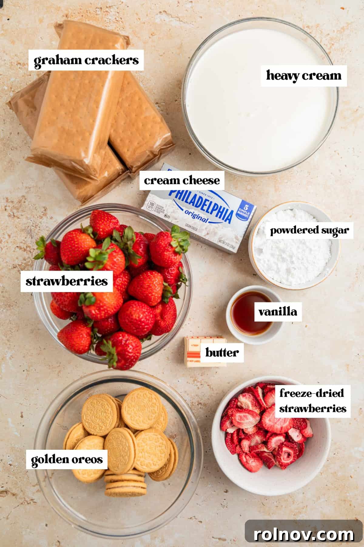 No-Bake Strawberry Dream Cake 3 Various ingredients for Strawberry Cream Cheese Icebox Cake laid out on a surface, including graham crackers, heavy whipping cream, vanilla extract, a block of cream cheese, and sliced fresh strawberries.