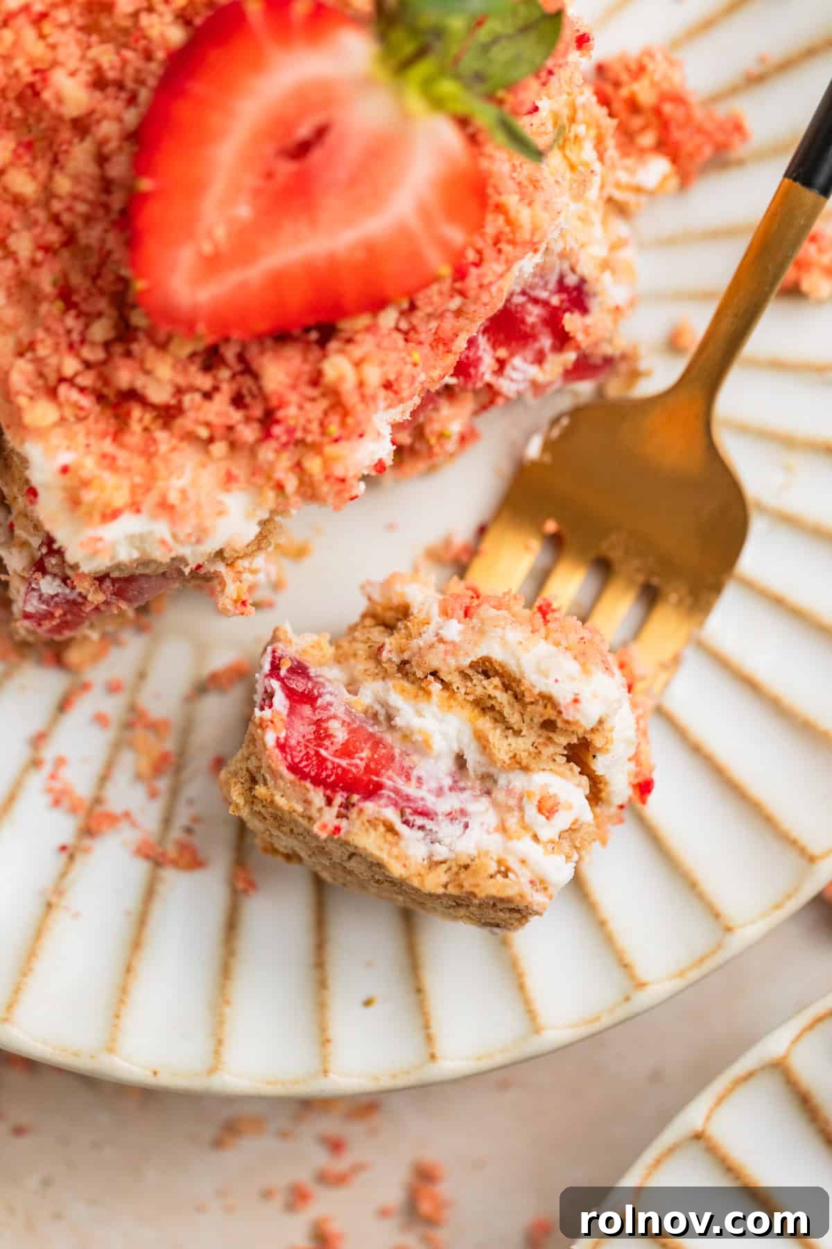 No-Bake Strawberry Dream Cake 9 A fork taking a bite of a layered Strawberry Cream Cheese Icebox Cake, highlighting the rich cream, fresh strawberries, and irresistible strawberry crunch topping on a white plate.