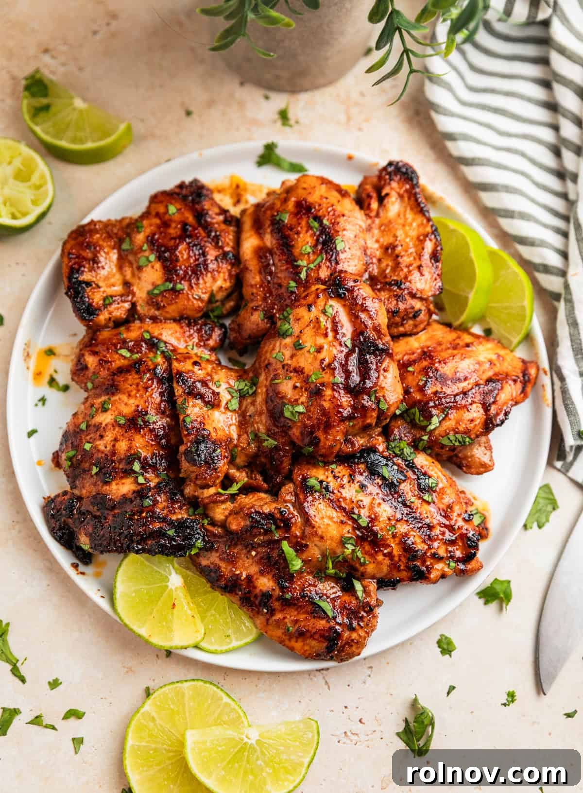 Grilled chicken thighs on white plate with sliced limes.