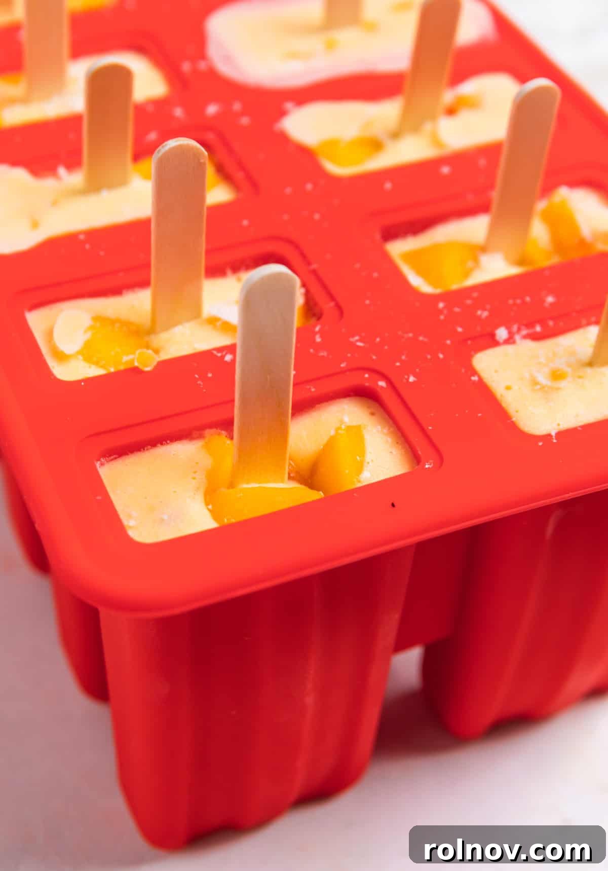 Peaches & Cream Pops 6 Popsicle mold filled with peaches and cream blended mixture and popsicle sticks inserted.