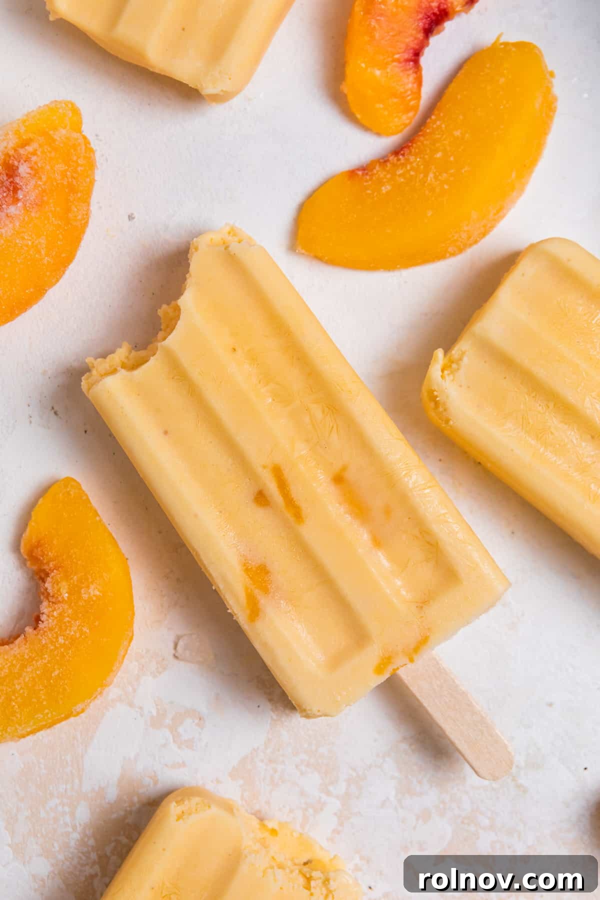 Peaches & Cream Pops 7 Peach popsicle on counter with peach slices surrounding.