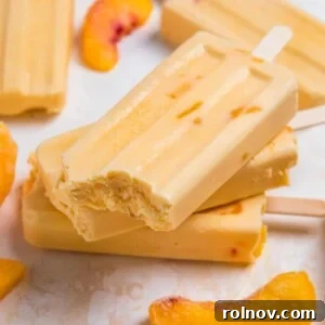 Creamy peach popsicles stacked with bite taken out of top popsicle.