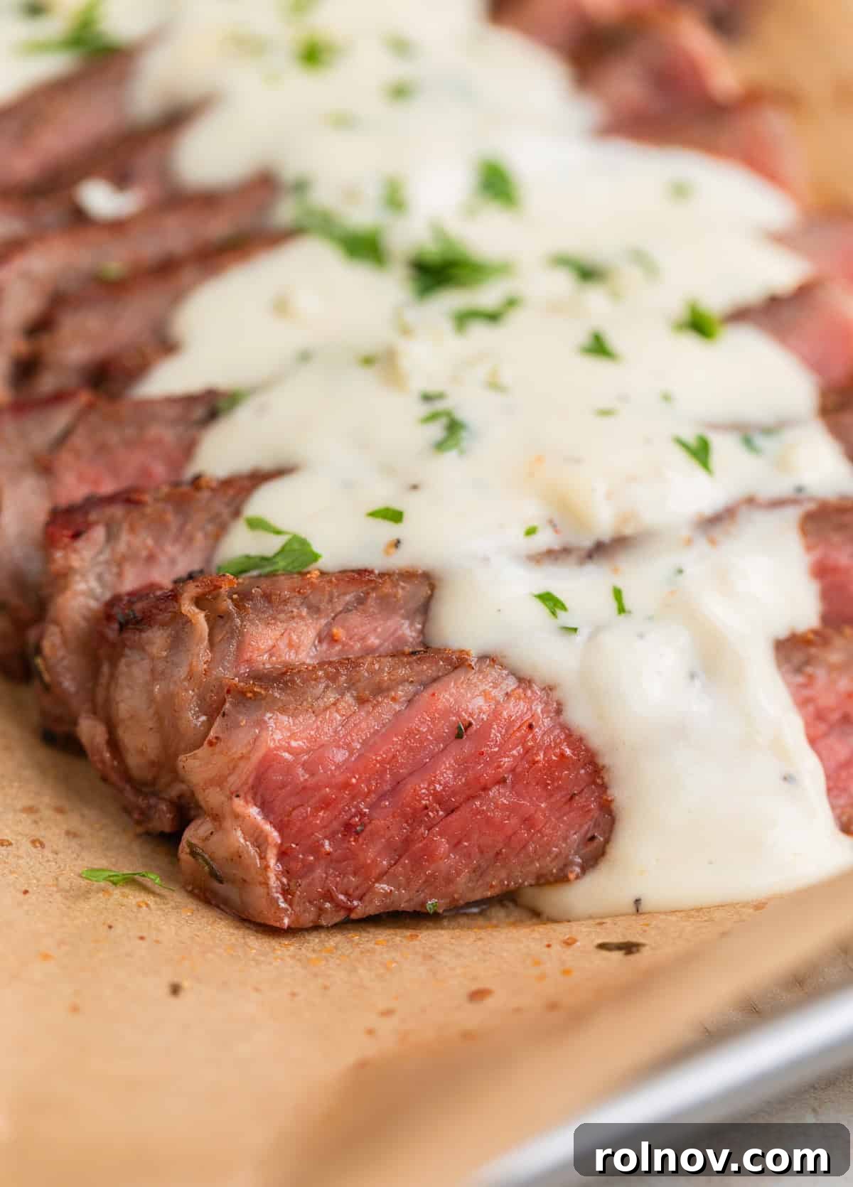 Ribeye Perfection with Gorgonzola Cream 10 Sliced ribeye steak on parchment paper with cream sauce over top.