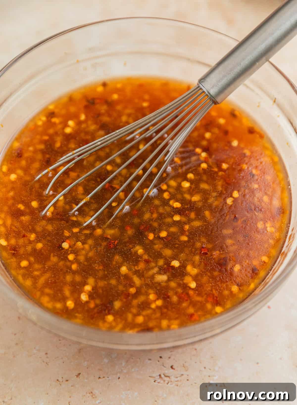 Zesty Slow Cooker Orange Chicken 5 A glass bowl containing whisked orange sauce, with a whisk resting inside, showing the smooth consistency.