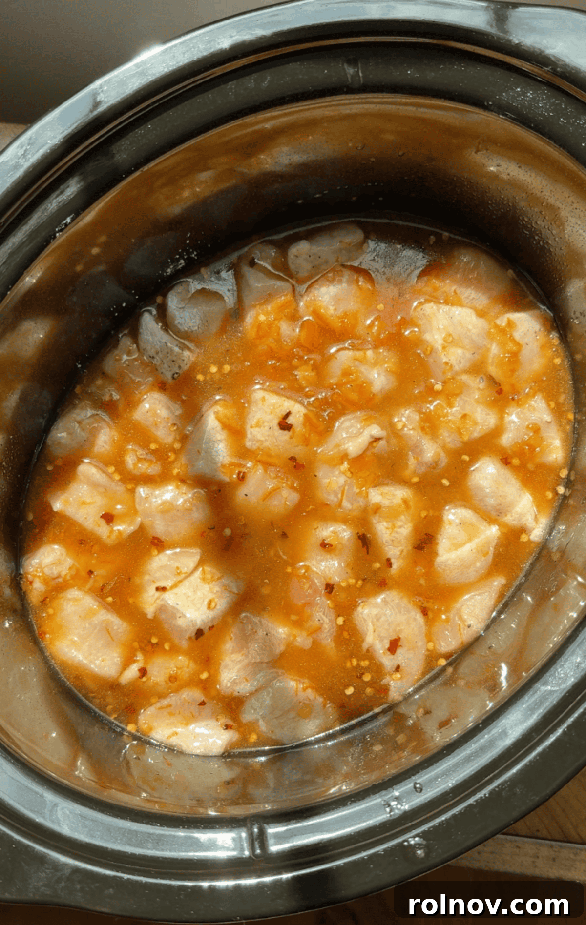Zesty Slow Cooker Orange Chicken 8 The remaining orange sauce being generously poured over the cornstarch-coated chicken in the slow cooker, ensuring good coverage.