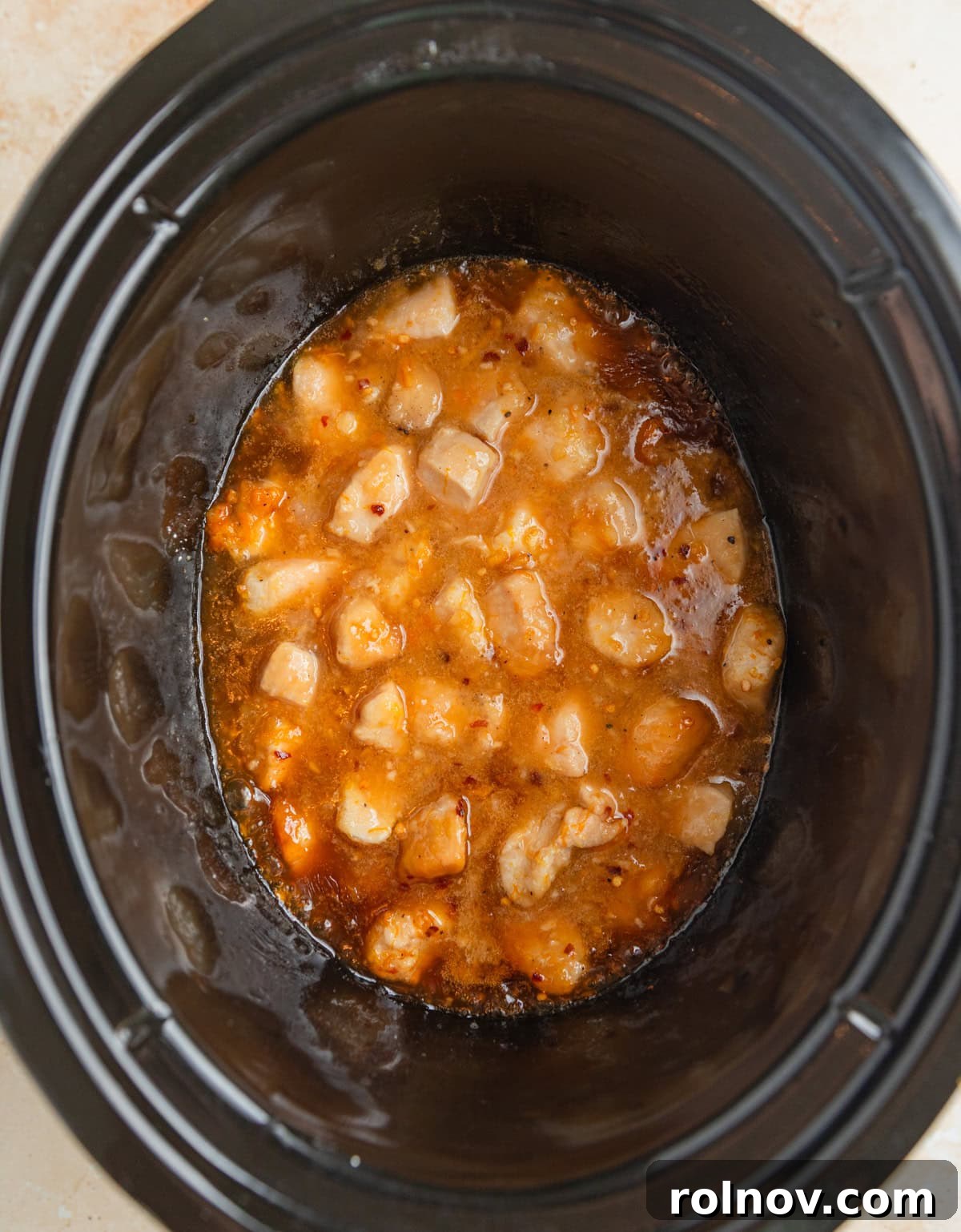 Zesty Slow Cooker Orange Chicken 9 Perfectly cooked orange chicken simmering in the slow cooker, coated in a thick, glossy orange sauce.