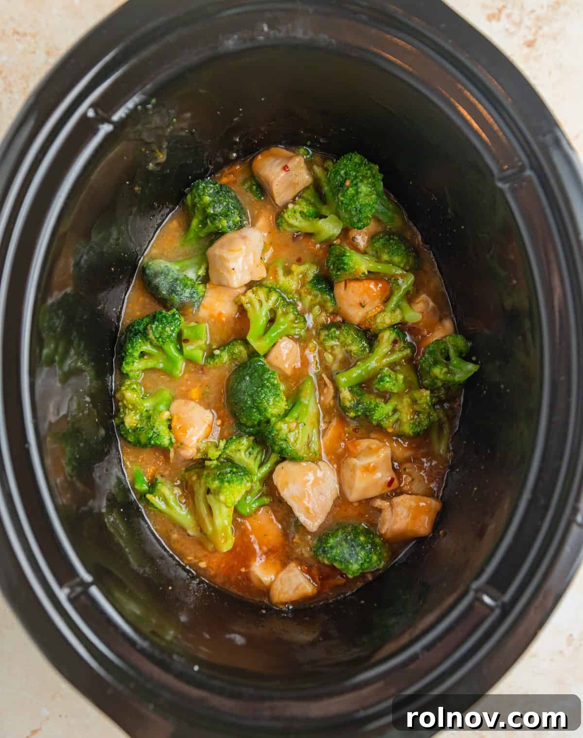 Zesty Slow Cooker Orange Chicken 10 Frozen broccoli florets being added to the cooked orange chicken simmering in the slow cooker.