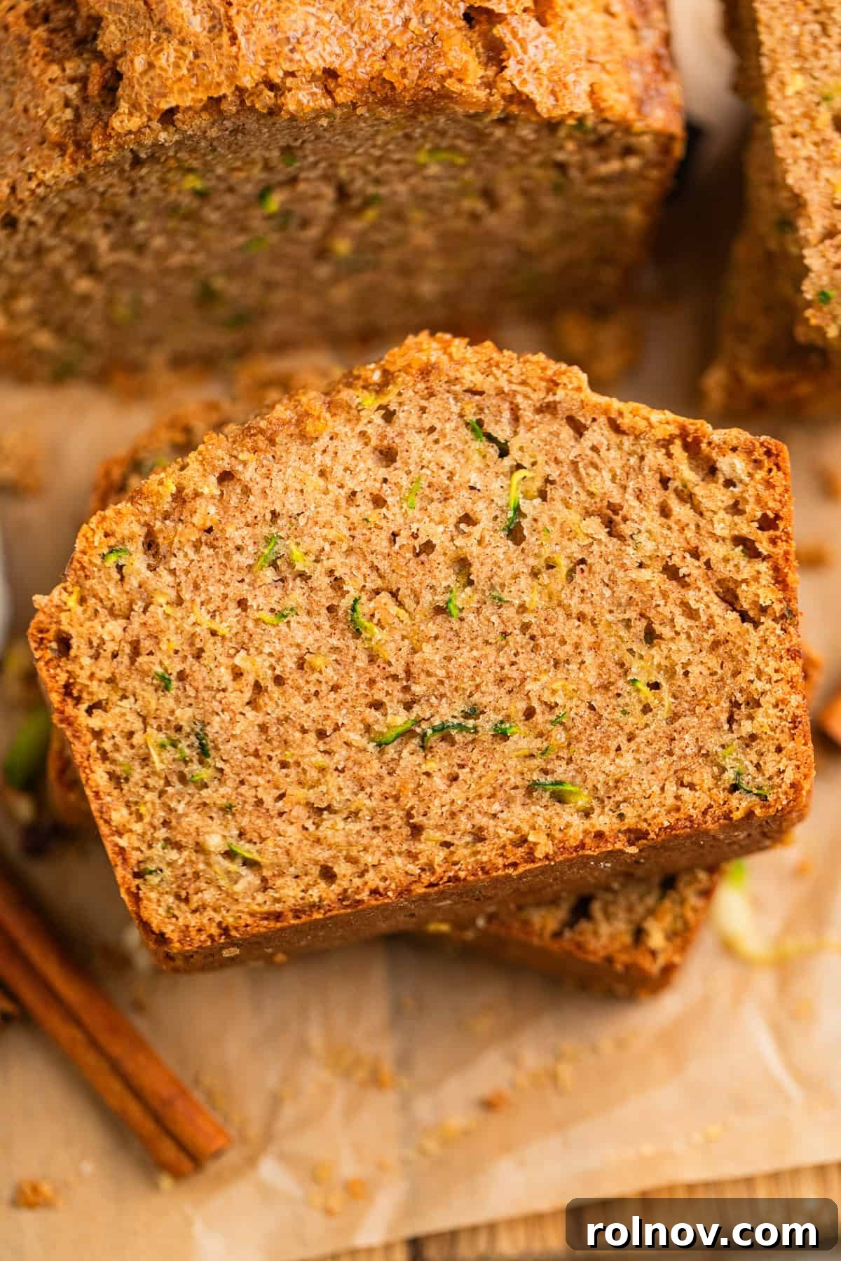 Grandmas Zucchini Bread Perfected 2 Freshly baked slices of zucchini bread arranged on parchment paper, with aromatic cinnamon sticks beside them.
