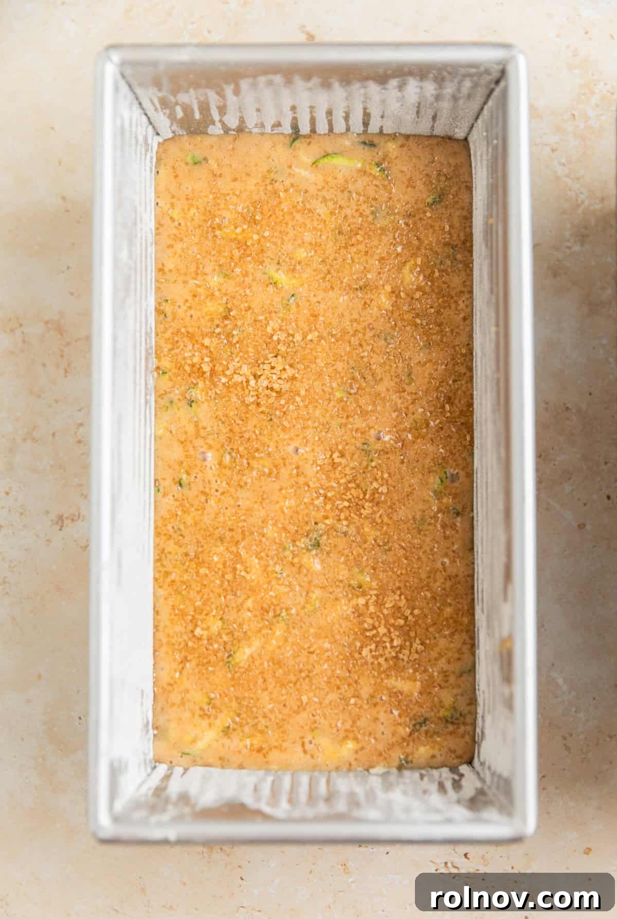Grandmas Zucchini Bread Perfected 12 Zucchini bread batter, topped with a generous layer of coarse sugar, evenly distributed in a loaf pan, ready for baking.