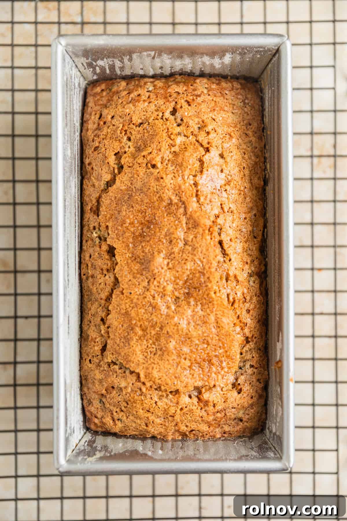 Grandmas Zucchini Bread Perfected 13 A perfectly golden-brown loaf of zucchini bread, just out of the oven, resting in its pan on a cooling rack.