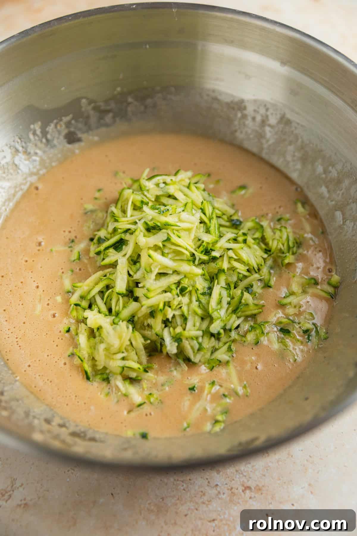 Grandmas Zucchini Bread Perfected 7 Freshly shredded zucchini being gently folded into the zucchini bread batter mixture in a glass bowl.