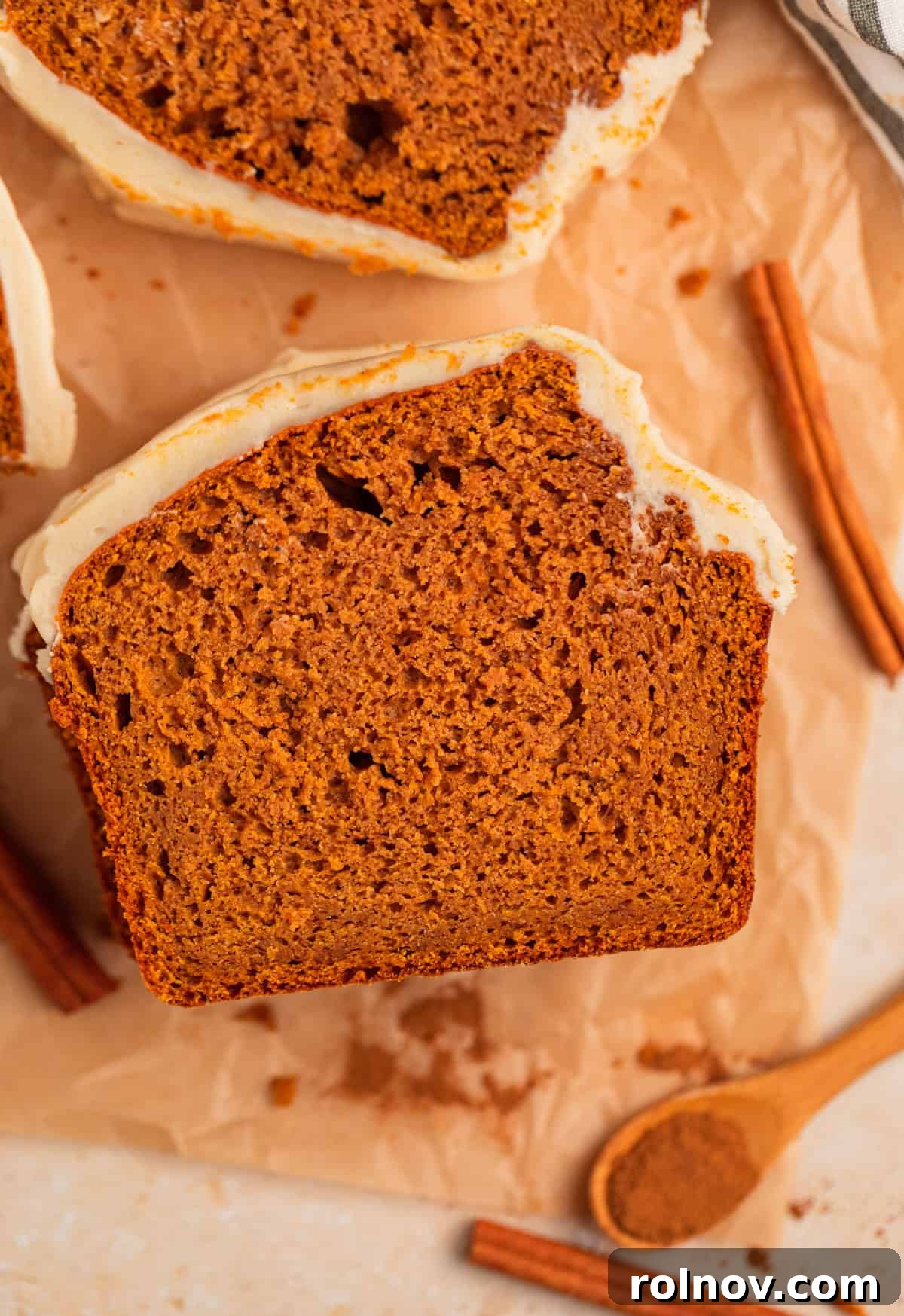 Effortless Cake Mix Pumpkin Bread 2 A perfectly sliced piece of cake mix pumpkin bread, generously topped with creamy brown sugar cream cheese frosting, resting on parchment paper.