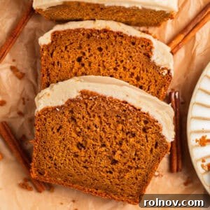 Effortless Cake Mix Pumpkin Bread 16 Frosted pumpkin bread slices on parchment with cinnamon sticks.