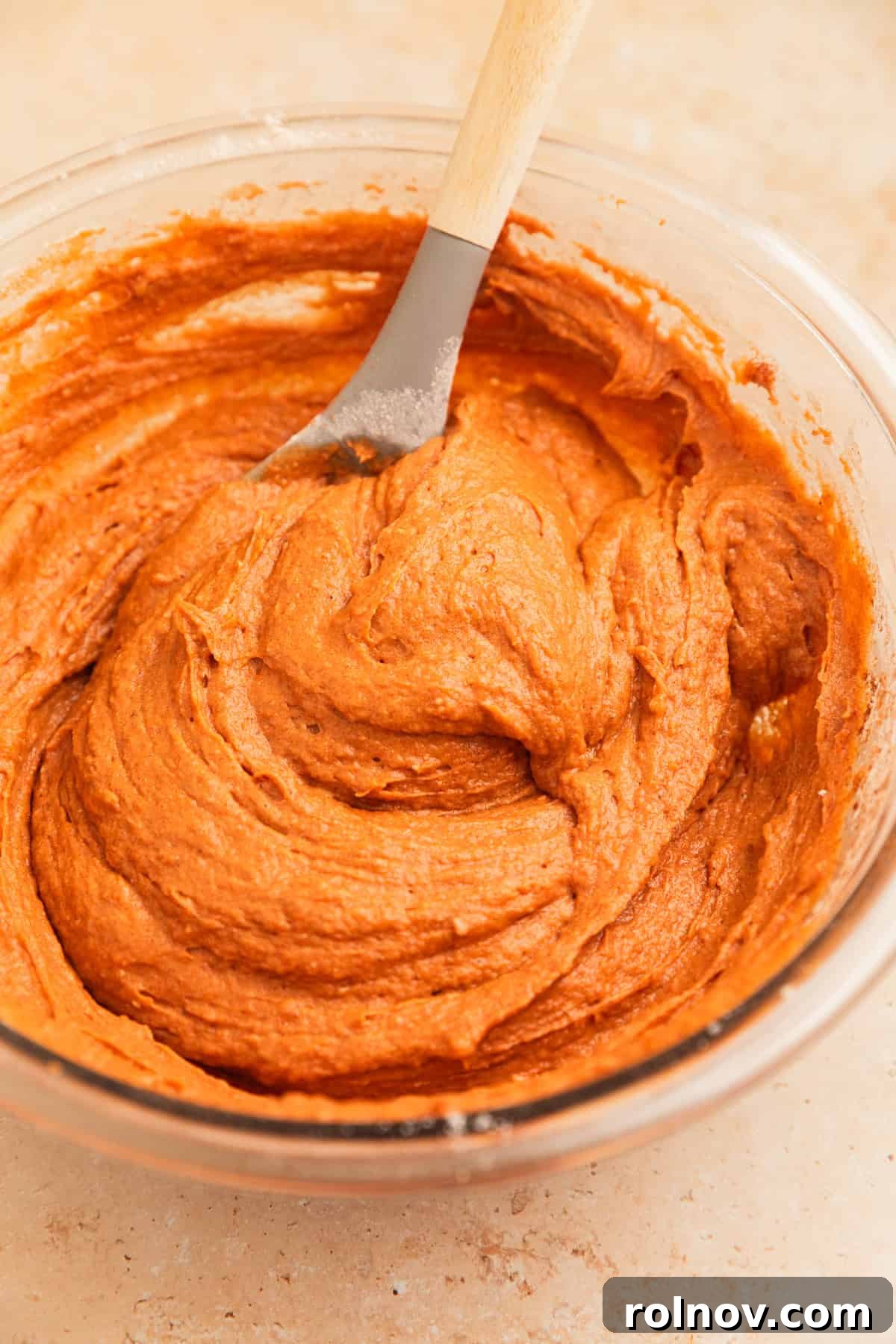 Effortless Cake Mix Pumpkin Bread 9 The cake mix pumpkin bread batter in a glass mixing bowl, gently stirred to combine with a spoon, showing a smooth consistency.