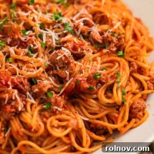 Plate with spaghetti tossed in meat sauce with parmesan and herbs over top.