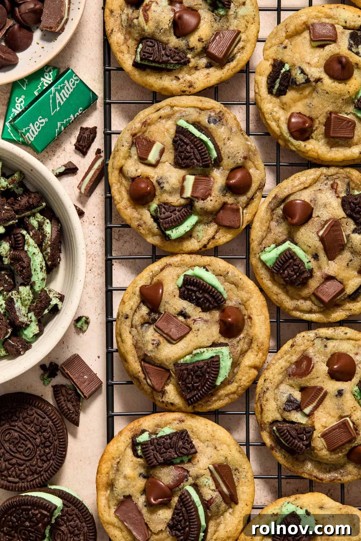 Cooling rack with freshly baked mint chocolate chip cookies, surrounded by mint Oreos, Andes mints, and chocolate chips.