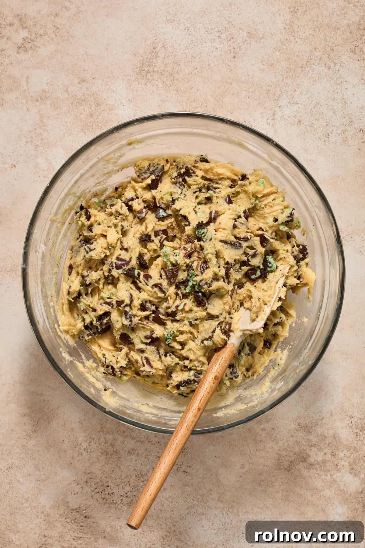 Fully mixed mint chocolate chip cookie dough in a mixing bowl with a spatula, showcasing its ready-to-chill consistency.